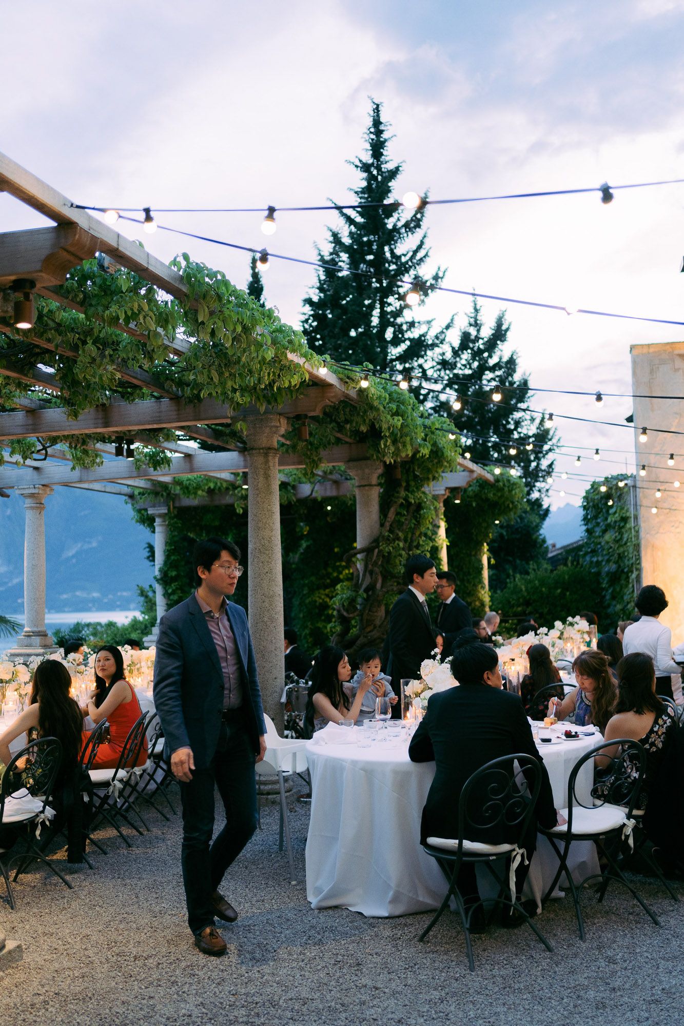 Guests enjoy an outdoor evening reception on a patio with string lights and mountain views in the background.