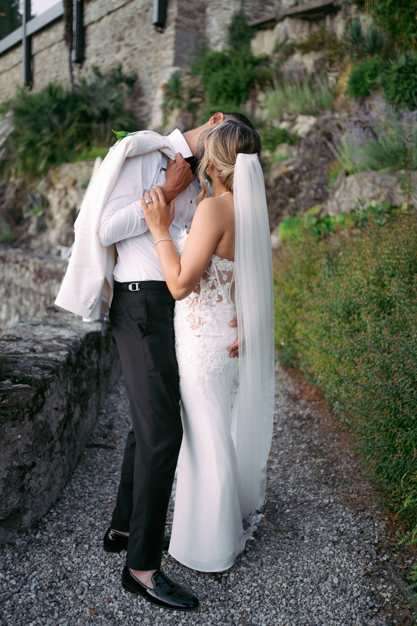 A romantic wedding couple shares intimate moments on a rustic stone path surrounded by greenery.