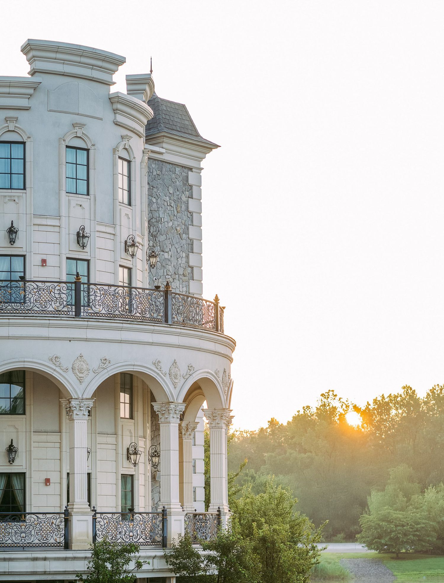 Elegant white mansion with ornate balcony and classical columns captures golden sunset through arched architecture.