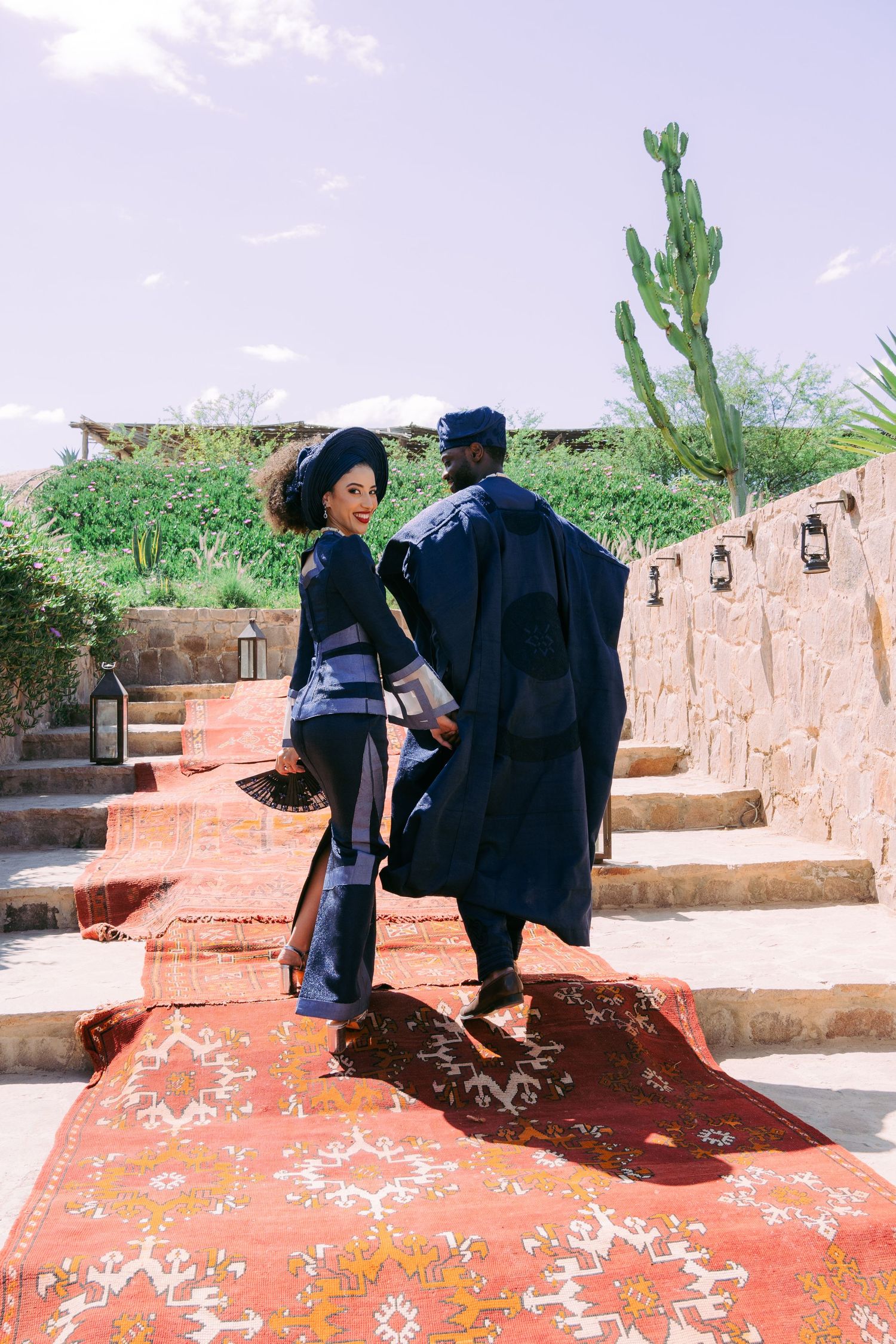 Couple walking on pink stone steps with a decorative rug and desert cactus in the background.