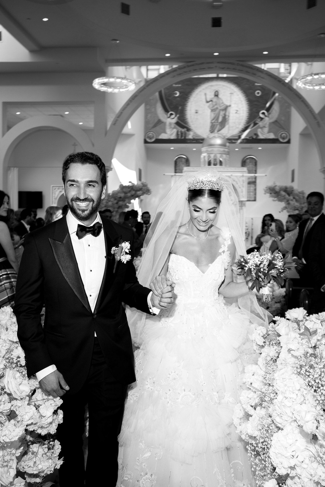 A sequence of black and white wedding ceremony photos showing a bride and groom walking down the aisle at their celebration.