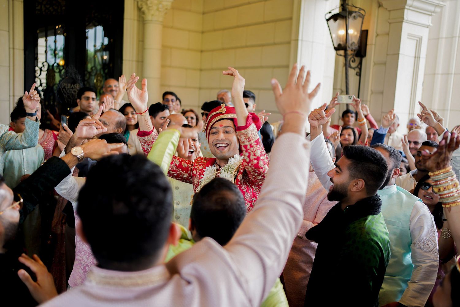 A large crowd of people in traditional Middle Eastern dress raise their arms in celebration during an indoor event.