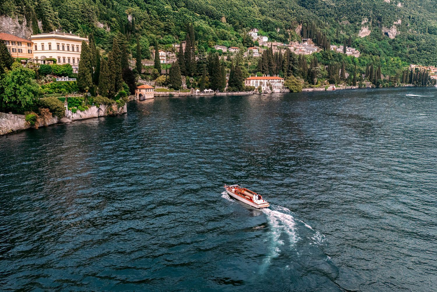 Scenic view of Lake Como in Italy with boats cruising past historic waterfront villas and lush green mountains.