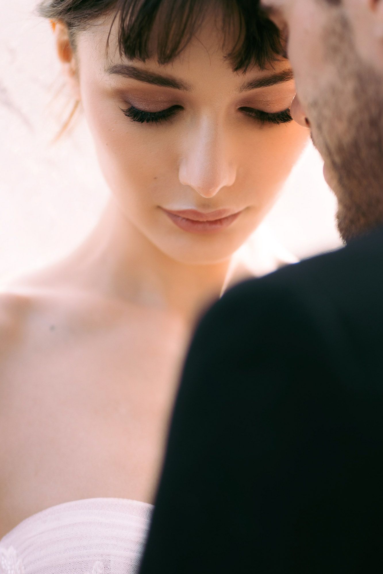 Close-up portrait of a bride with soft makeup and dark lashes looking down during an intimate wedding moment.