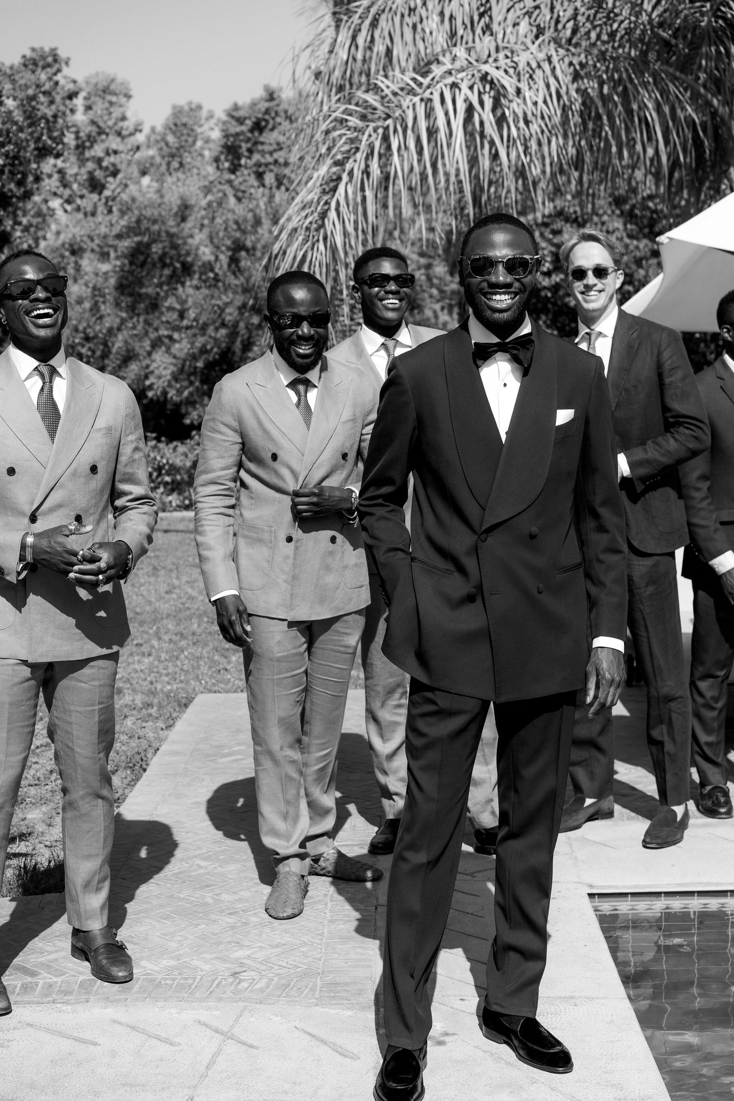 Black and white photo of groomsmen walking and laughing together by swimming pool.