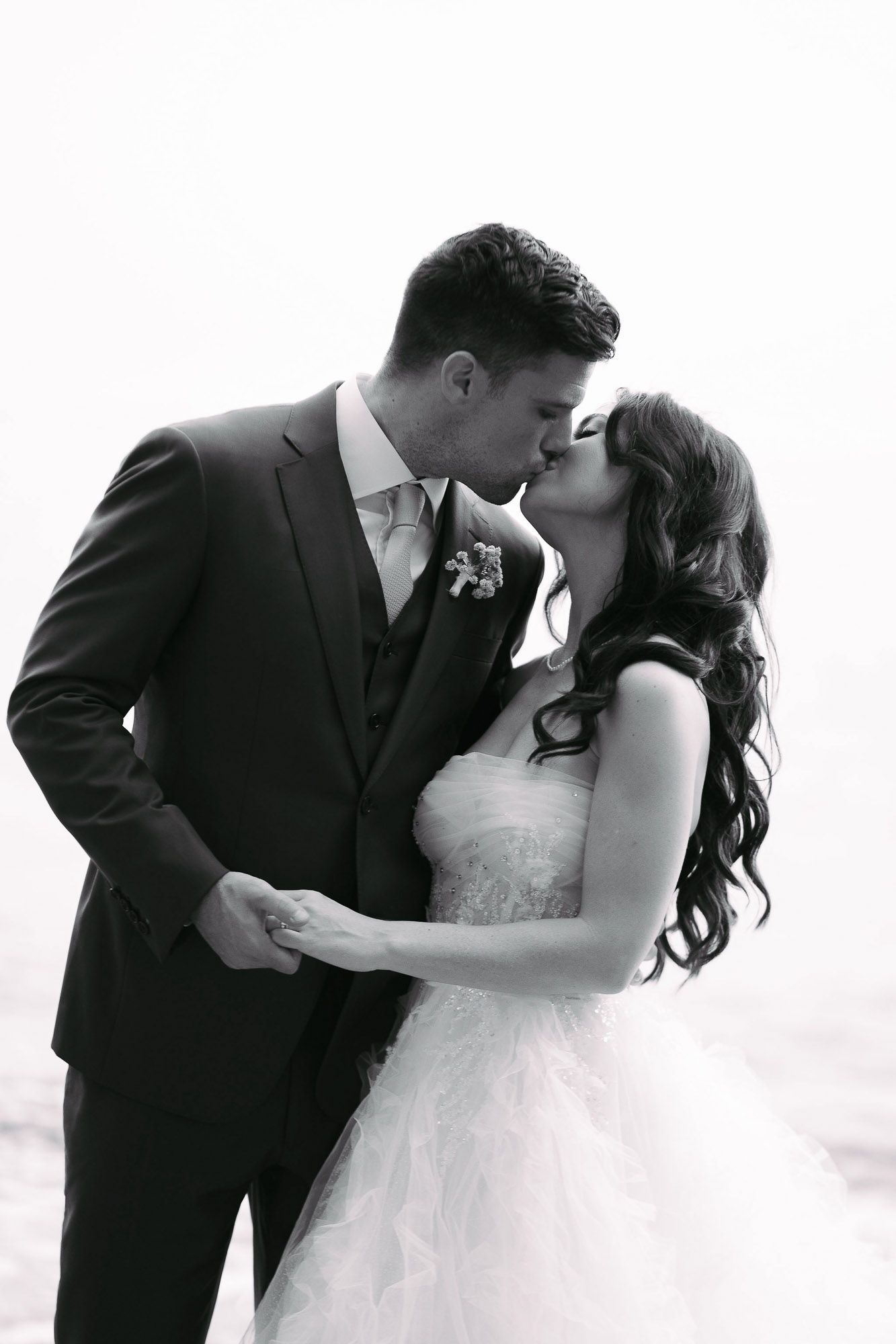 A romantic black and white wedding photo of a couple sharing a tender kiss in formal attire.