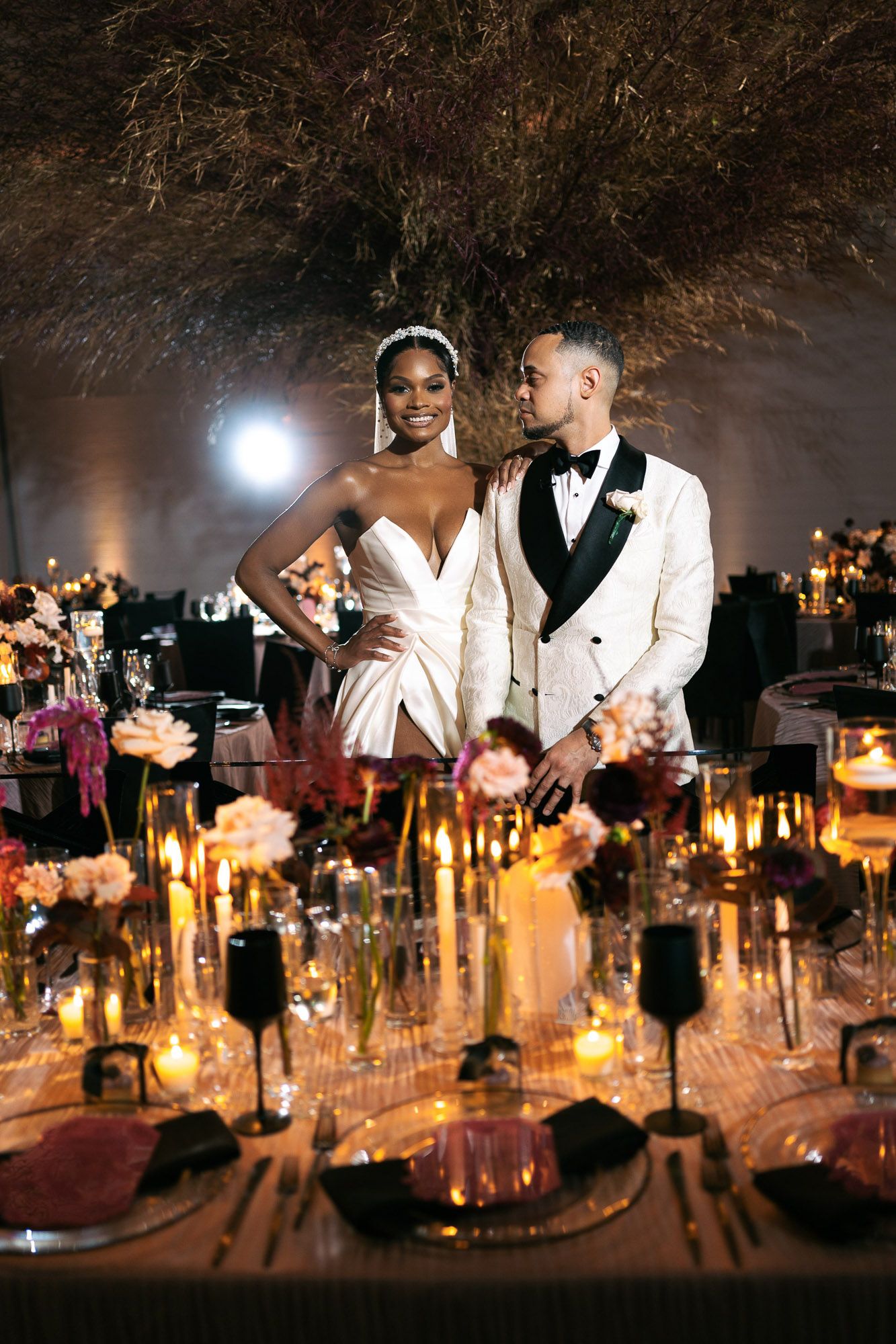 Candlelit wedding reception table decorated with elegant glassware and floral arrangements under evening sky.