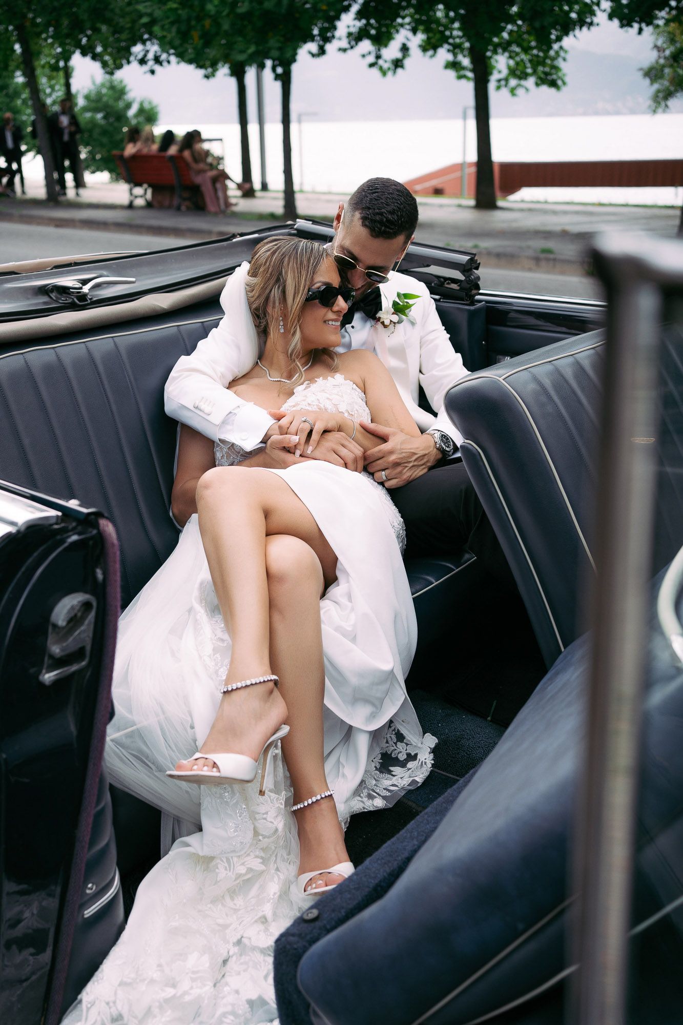A romantic moment captured in the back seat of a vintage car showing a couple in wedding attire.