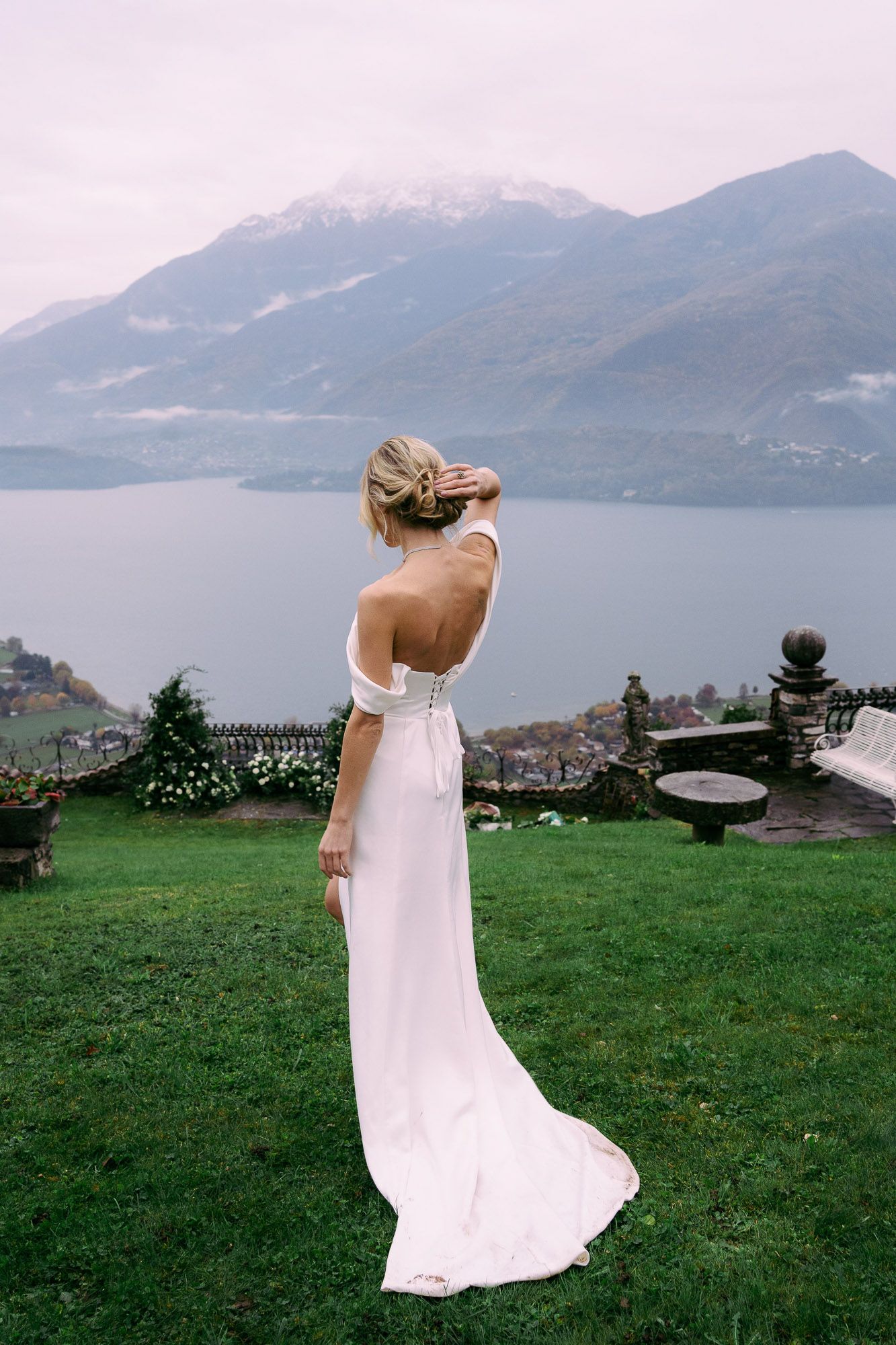 A flowing white dress catches the breeze against a scenic mountain lake backdrop on a grassy overlook.