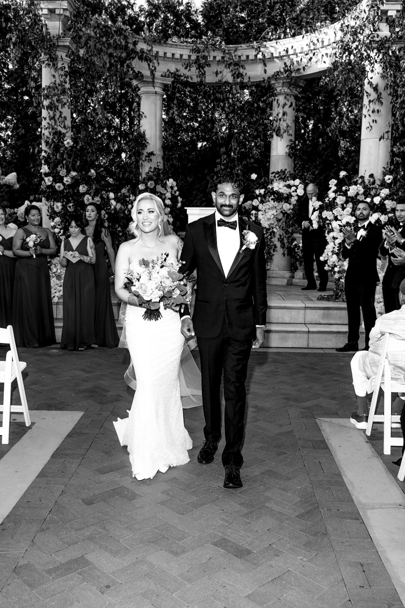 Black and white wedding ceremony photos showing couple walking down aisle in elegant venue with decorative columns.