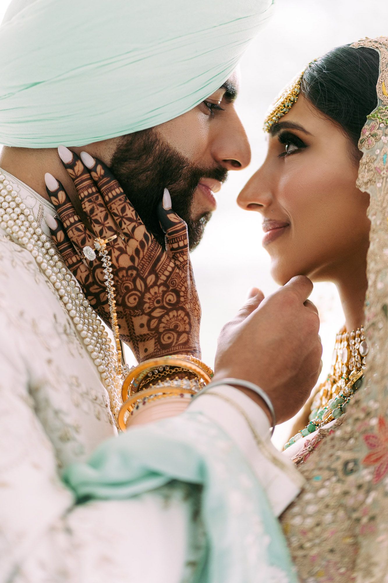 Intimate wedding portrait series showing traditional Sikh couple in mint and cream attire with intricate henna designs.