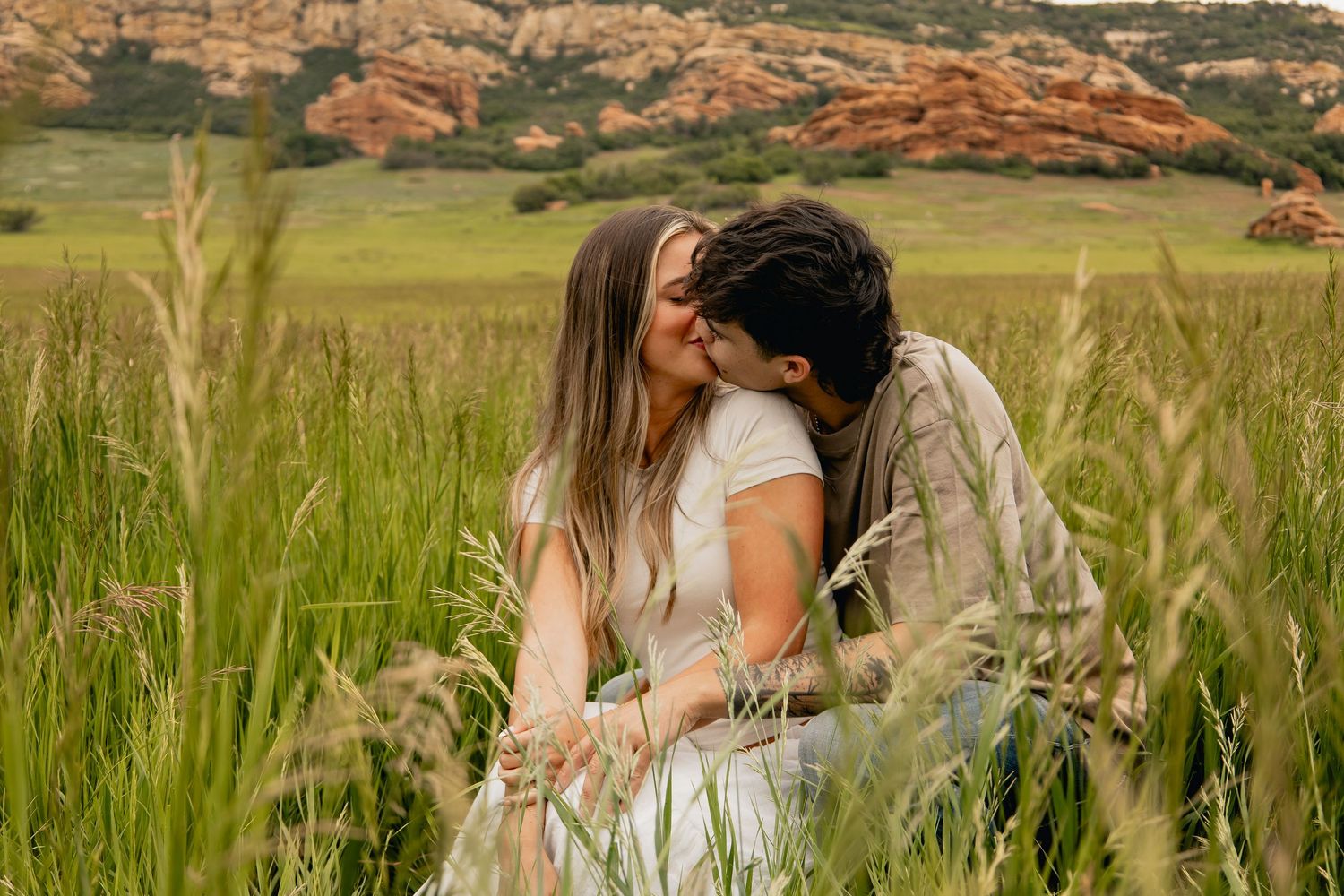 Couple sitting together in a lush green meadow during golden hour sharing a romantic moment.