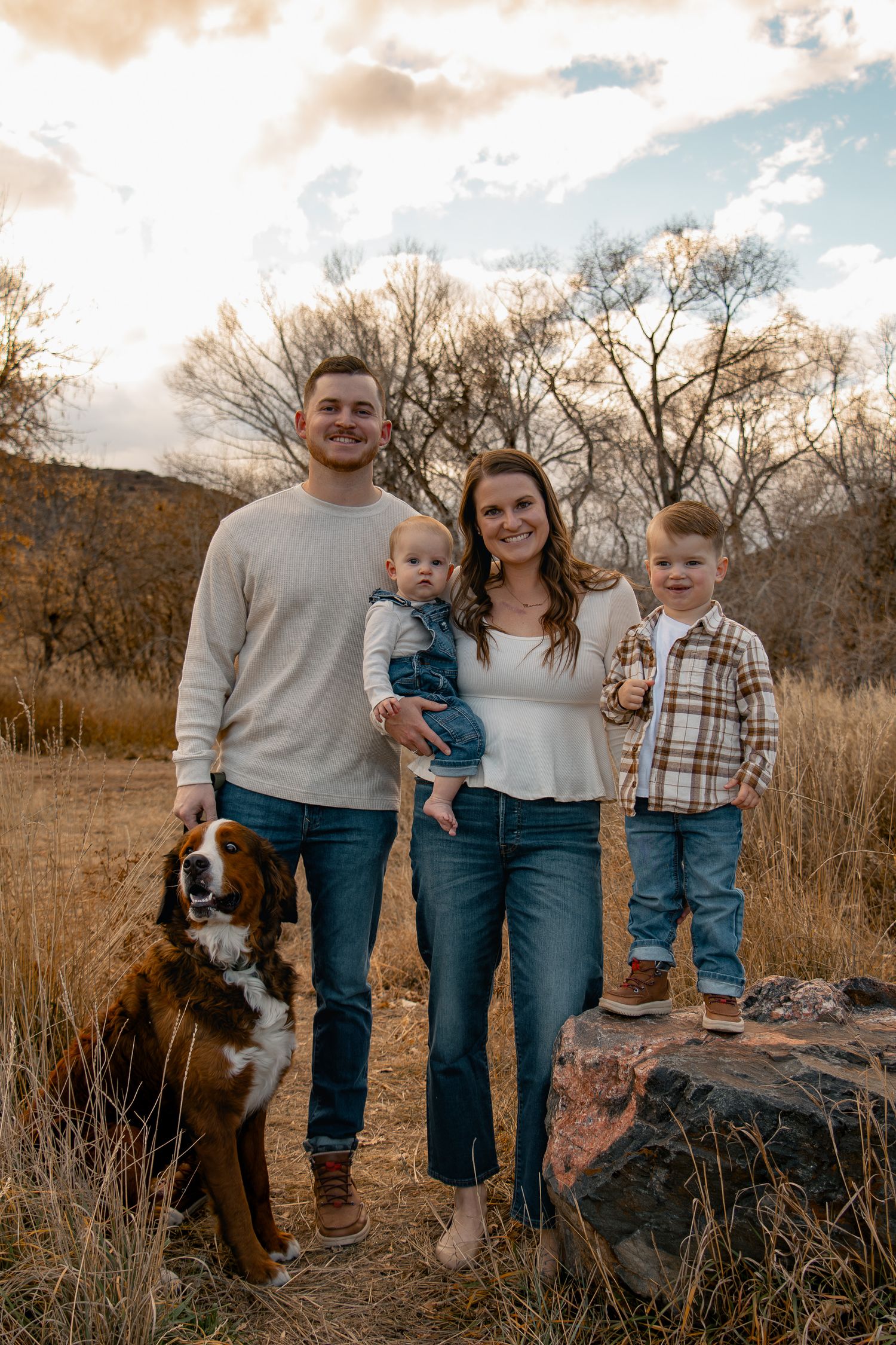 Family with young children poses together on rocks during golden hour in an autumn field setting.