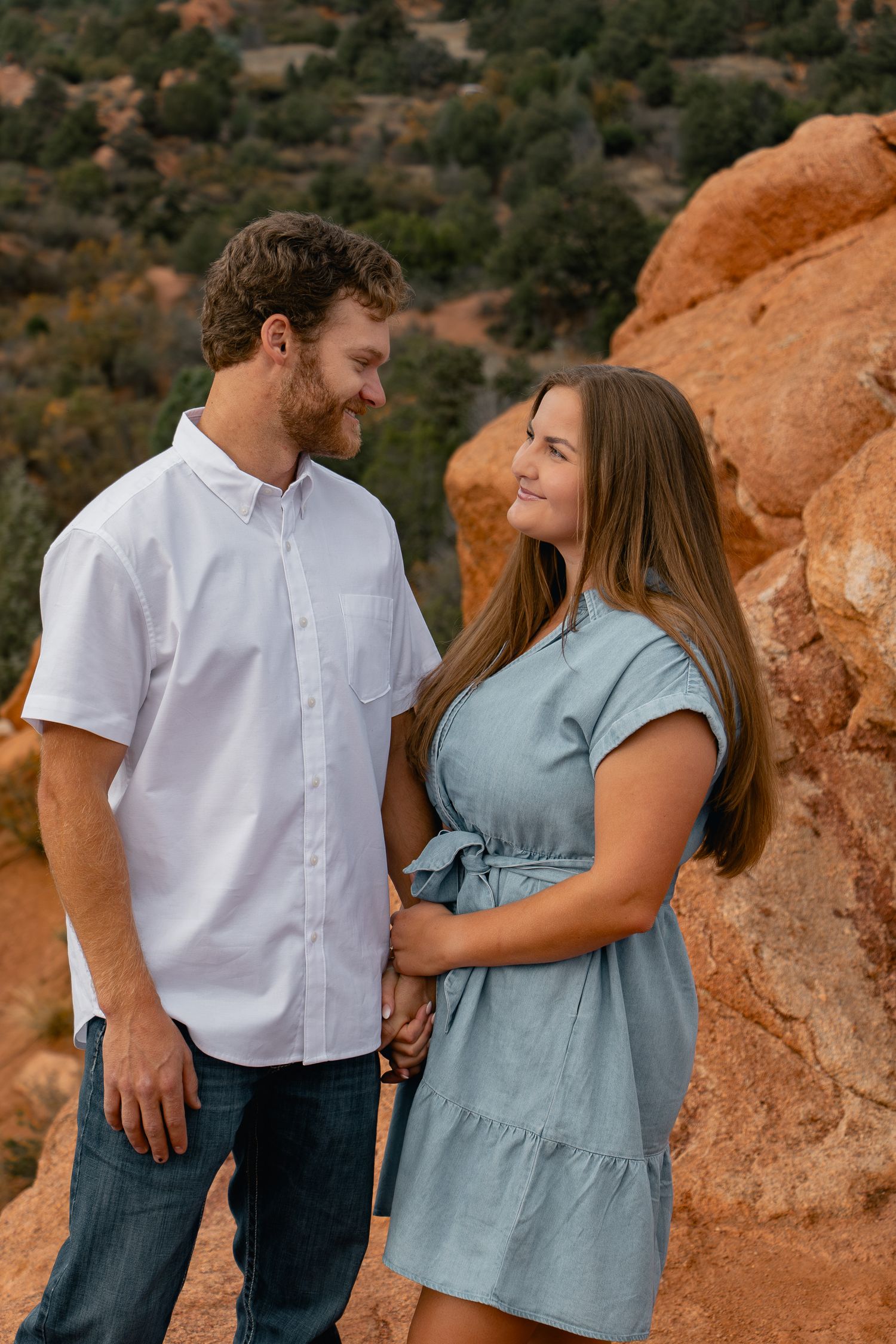 A couple shares an intimate moment while standing in front of orange rock formations in nature.