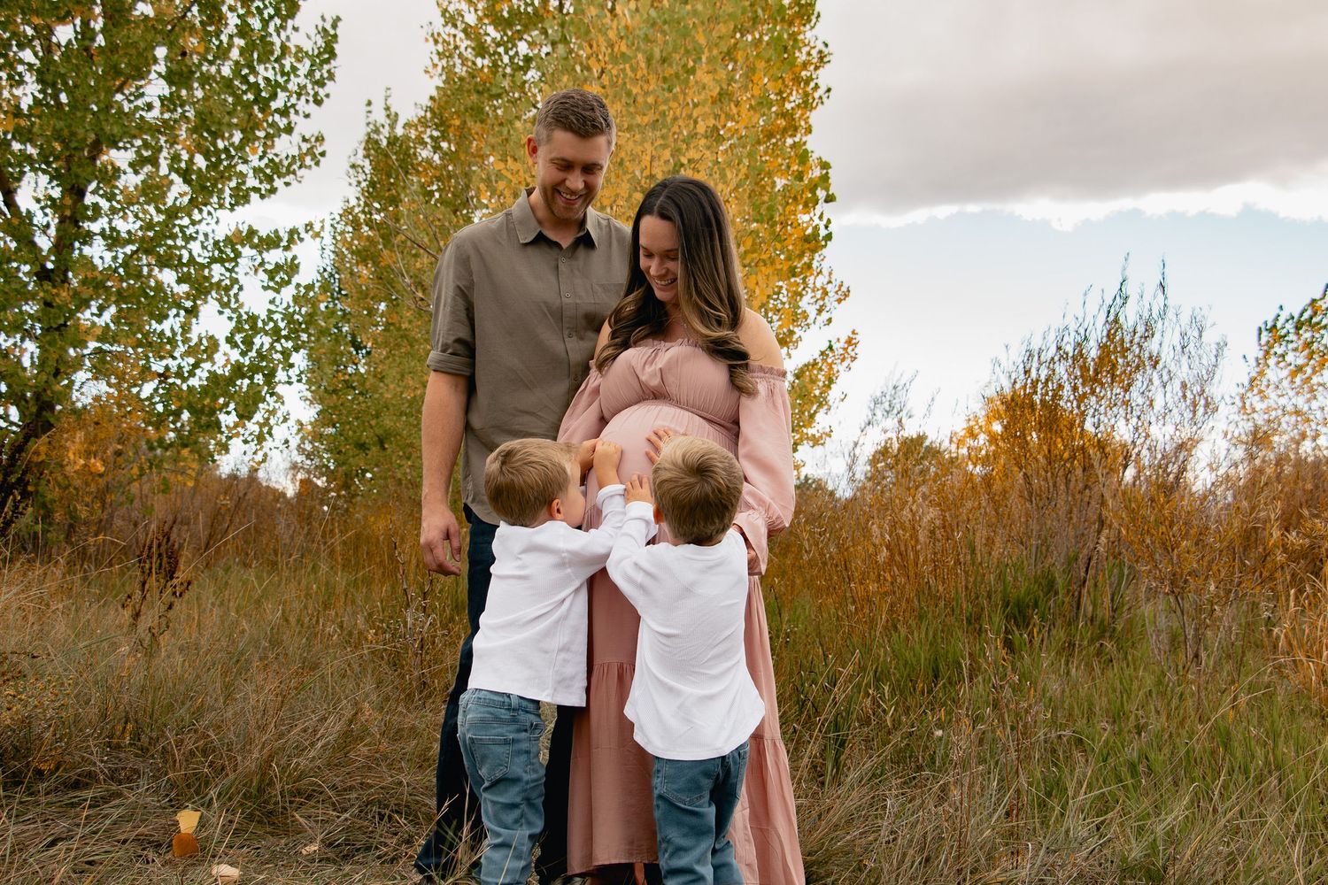 A couple shares an intimate moment in a golden autumn field with tall grass and trees in the background.