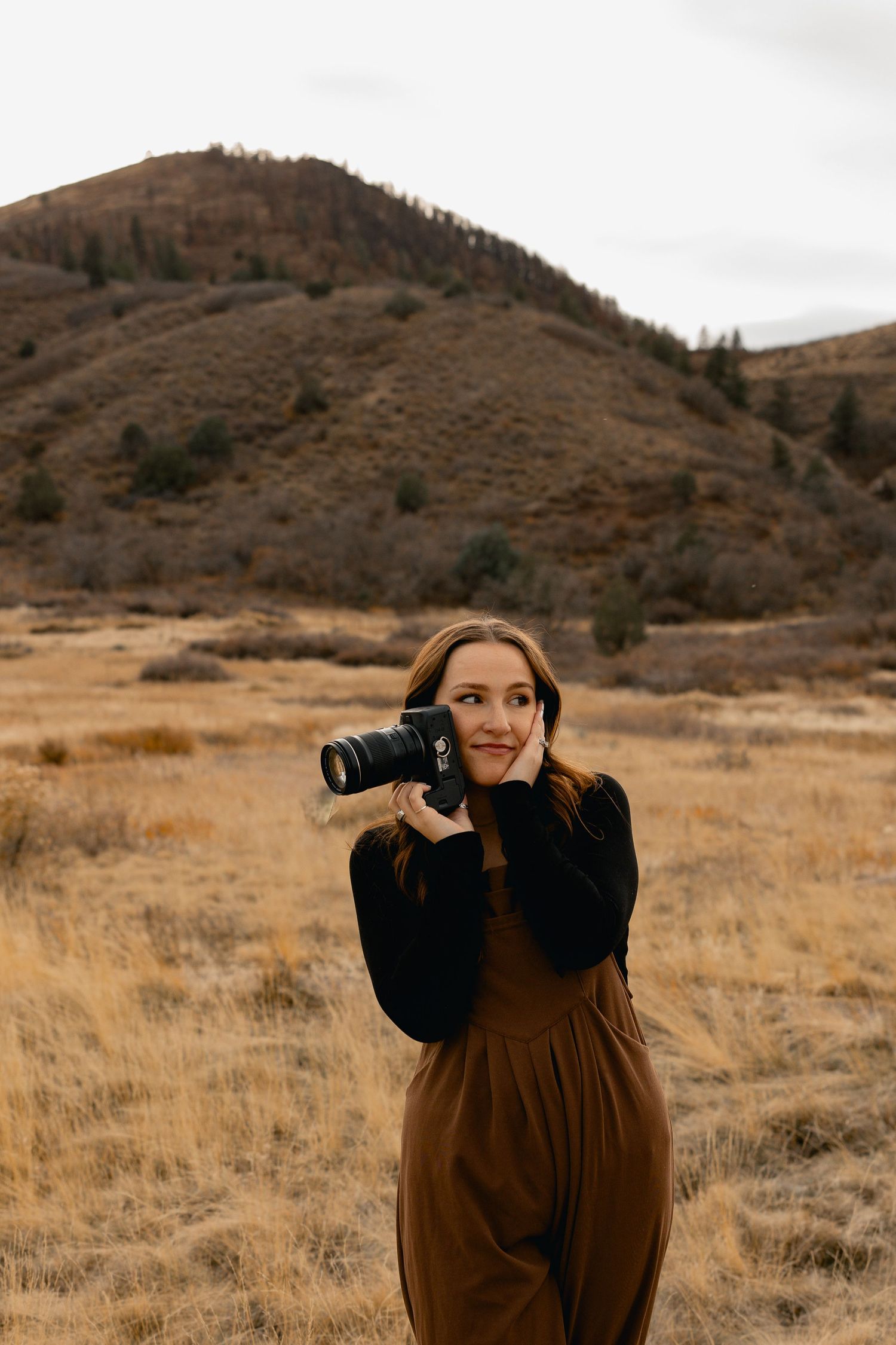 Photographer in brown dress taking pictures in a golden autumn field.