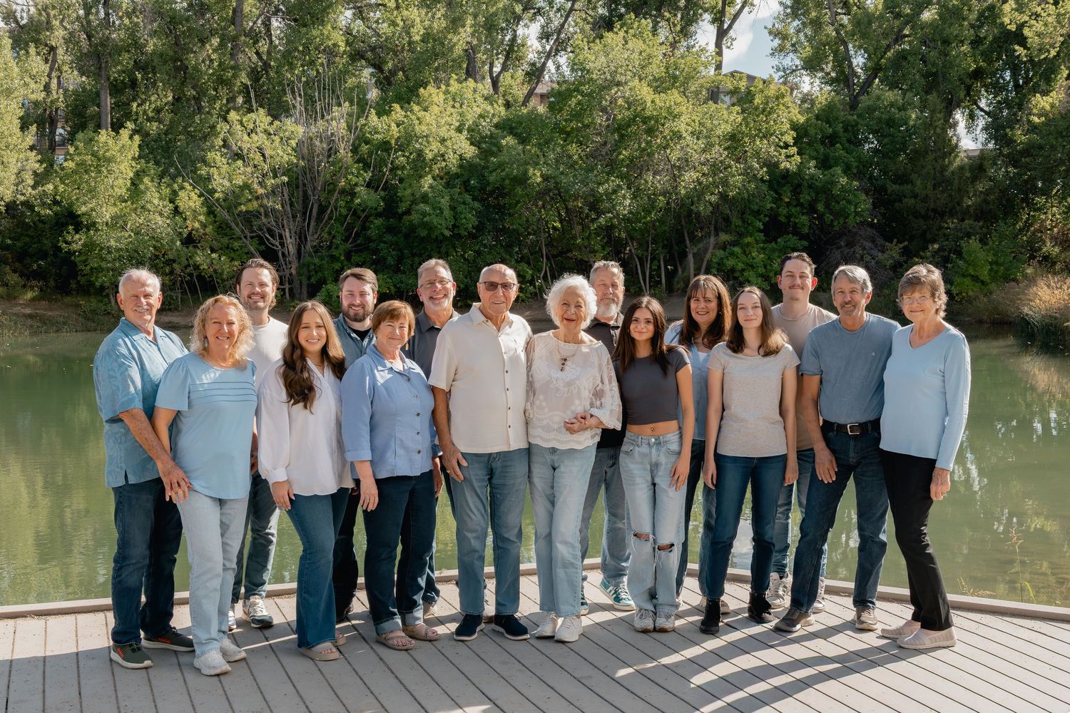 A large group wearing casual attire poses outdoors against a natural backdrop of trees and greenery.