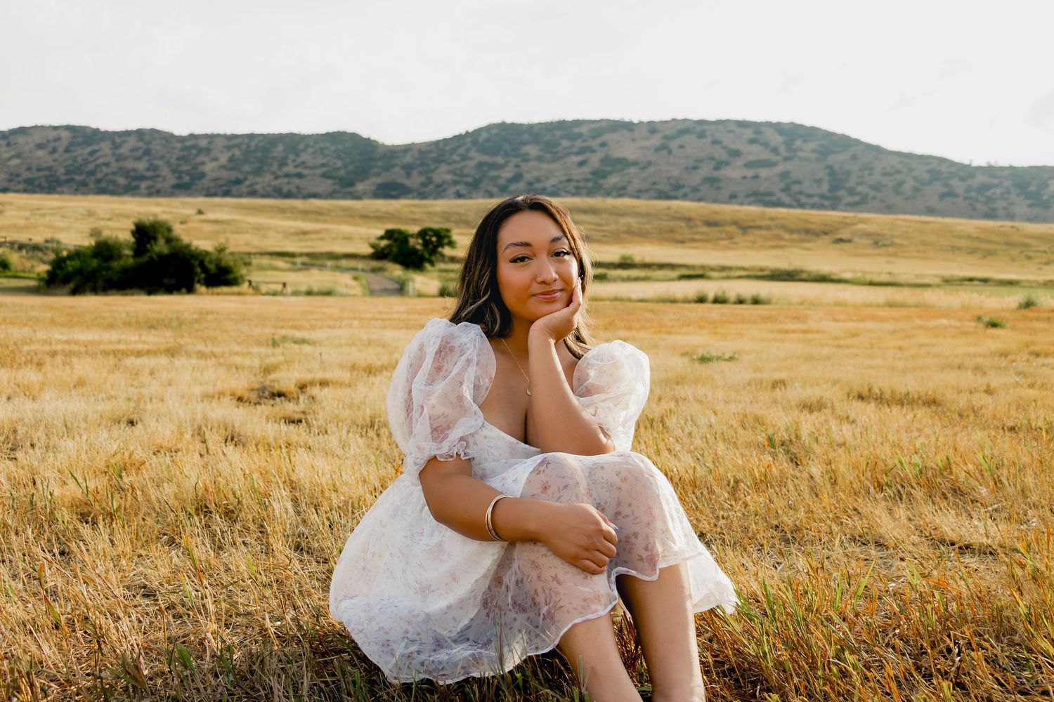 Person in ethereal white dress sits thoughtfully in golden prairie grass at sunset.