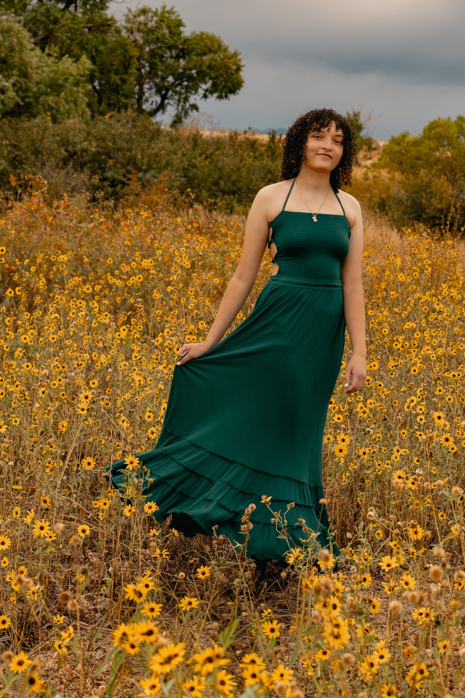 A person in an emerald green dress twirls gracefully among vibrant yellow wildflowers in a sunlit meadow.