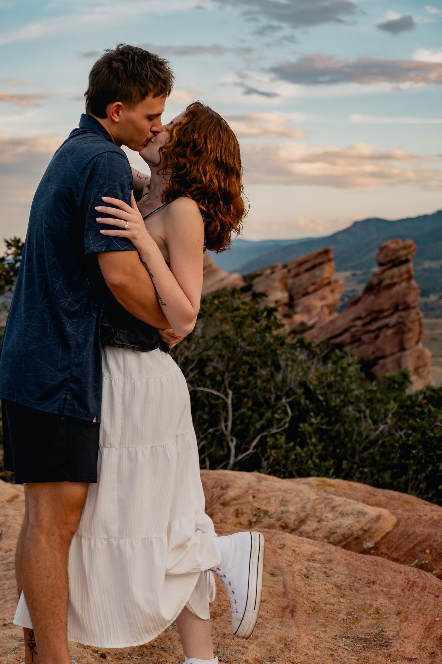 A romantic embrace at sunset against the backdrop of red rock formations at Red Rocks Park in Colorado.