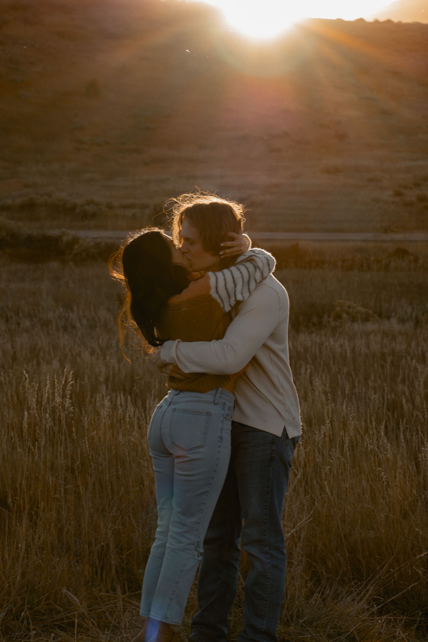 Silhouetted figures share an intimate moment against a warm sunset in a grassy field.
