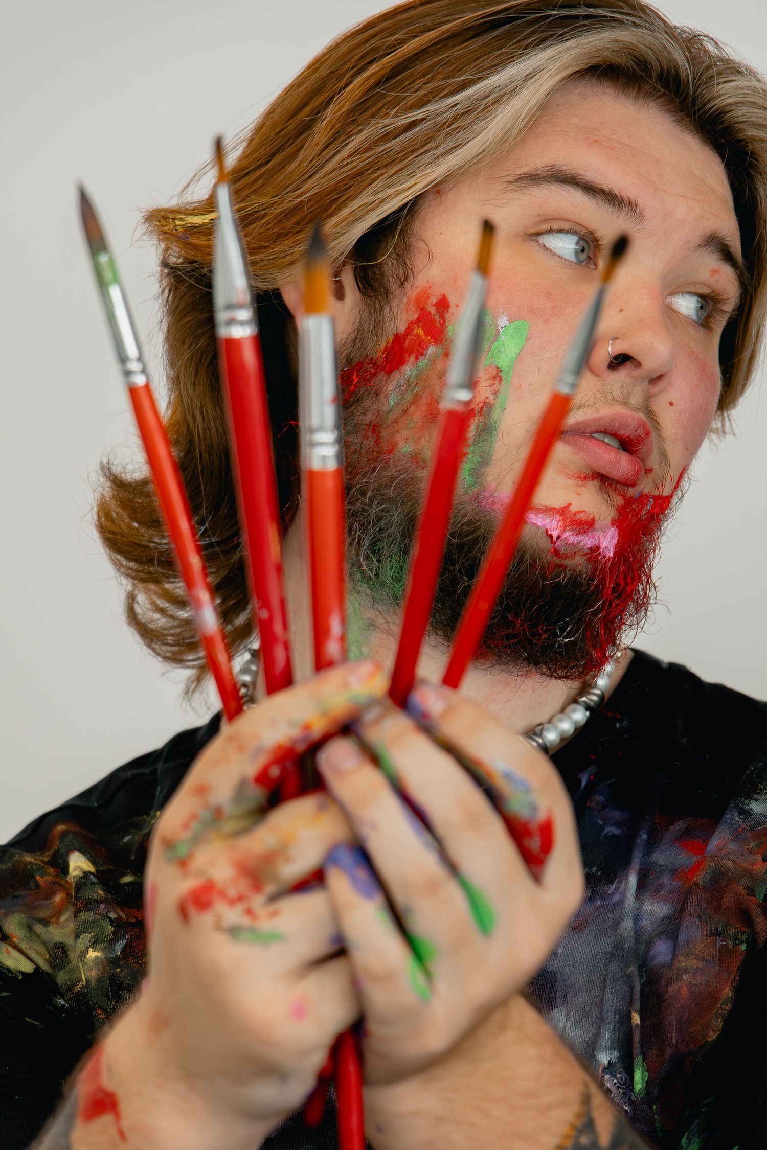 A series of artistic photos showing hands covered in paint with red pencils fanned between fingers against a white background.