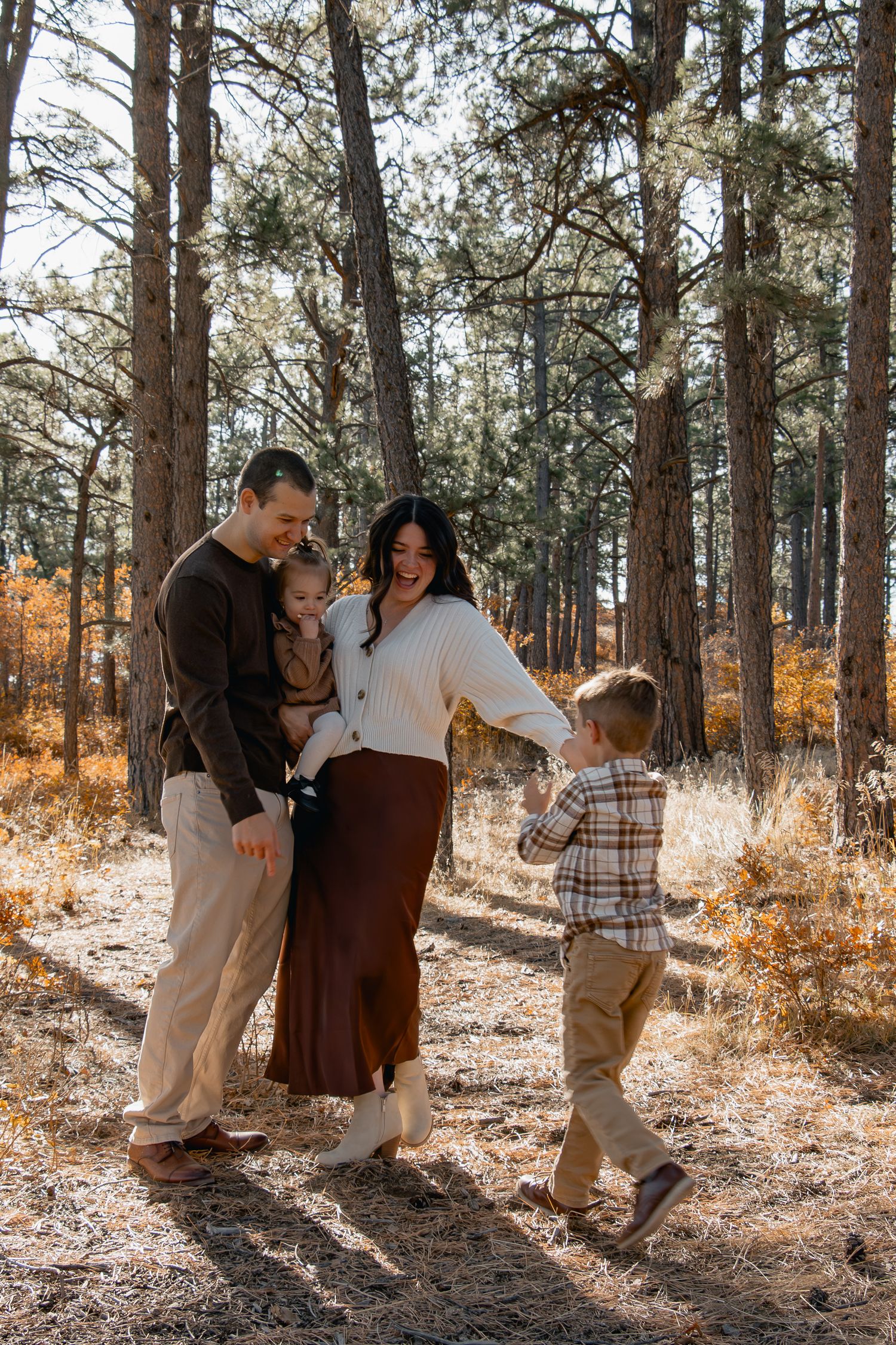 A family shares tender moments together in a sunlit forest setting during an autumn photo session.