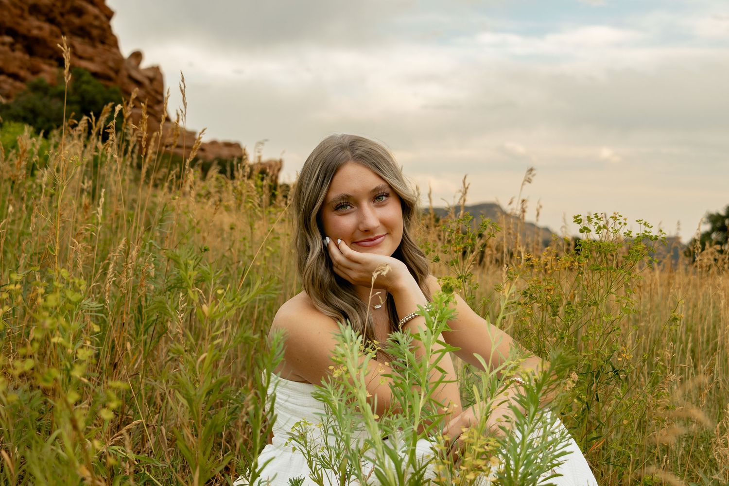 A woman wearing a floral top poses in a sunlit wildflower meadow.