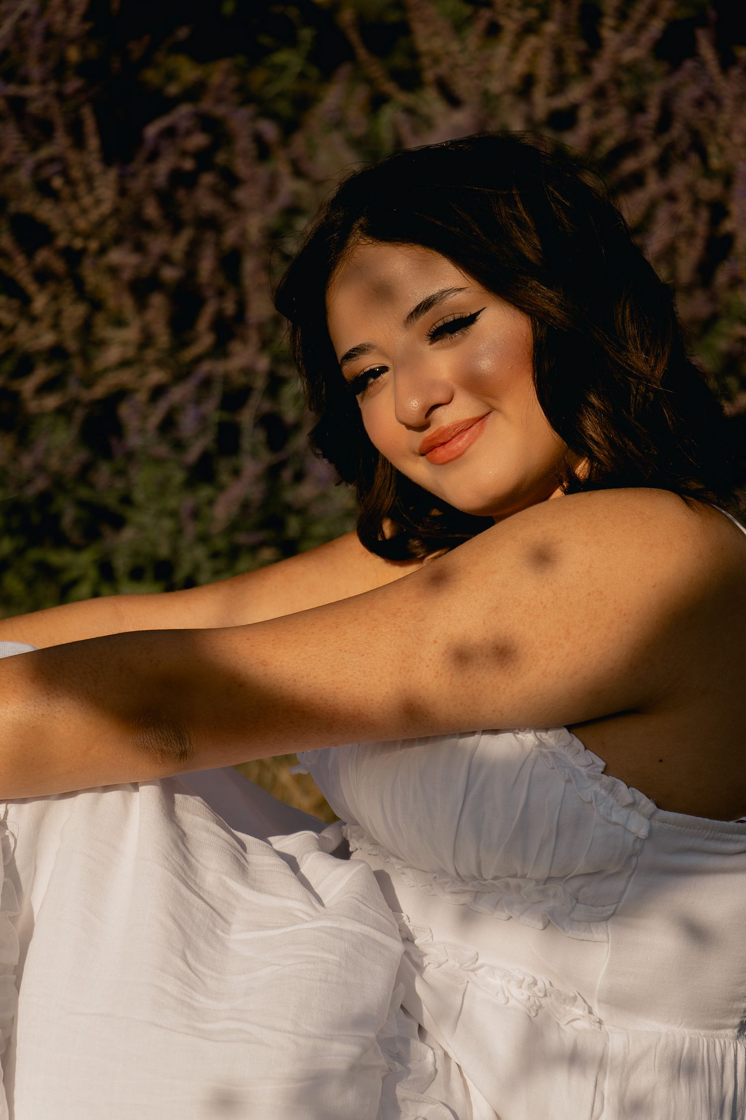 Portrait of someone in a white dress smiling warmly in golden sunlight against a natural background.