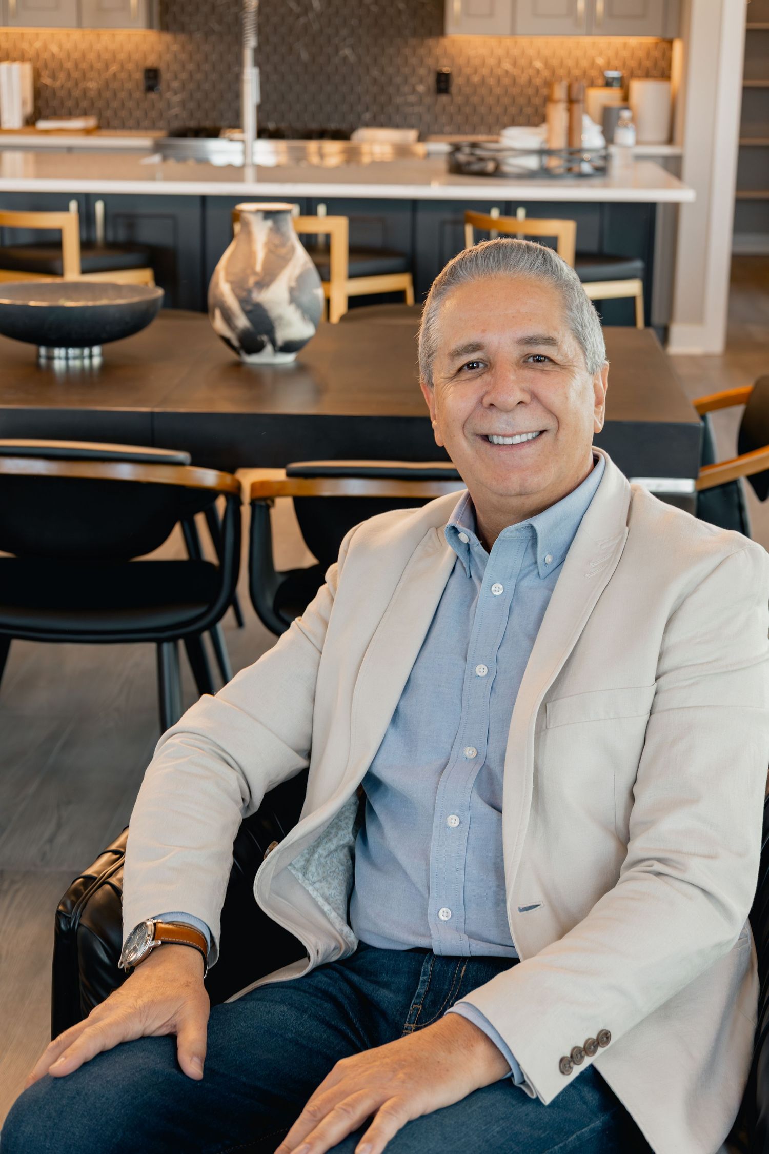 Professional in light blazer and blue button-down shirt sits casually in modern restaurant dining area.