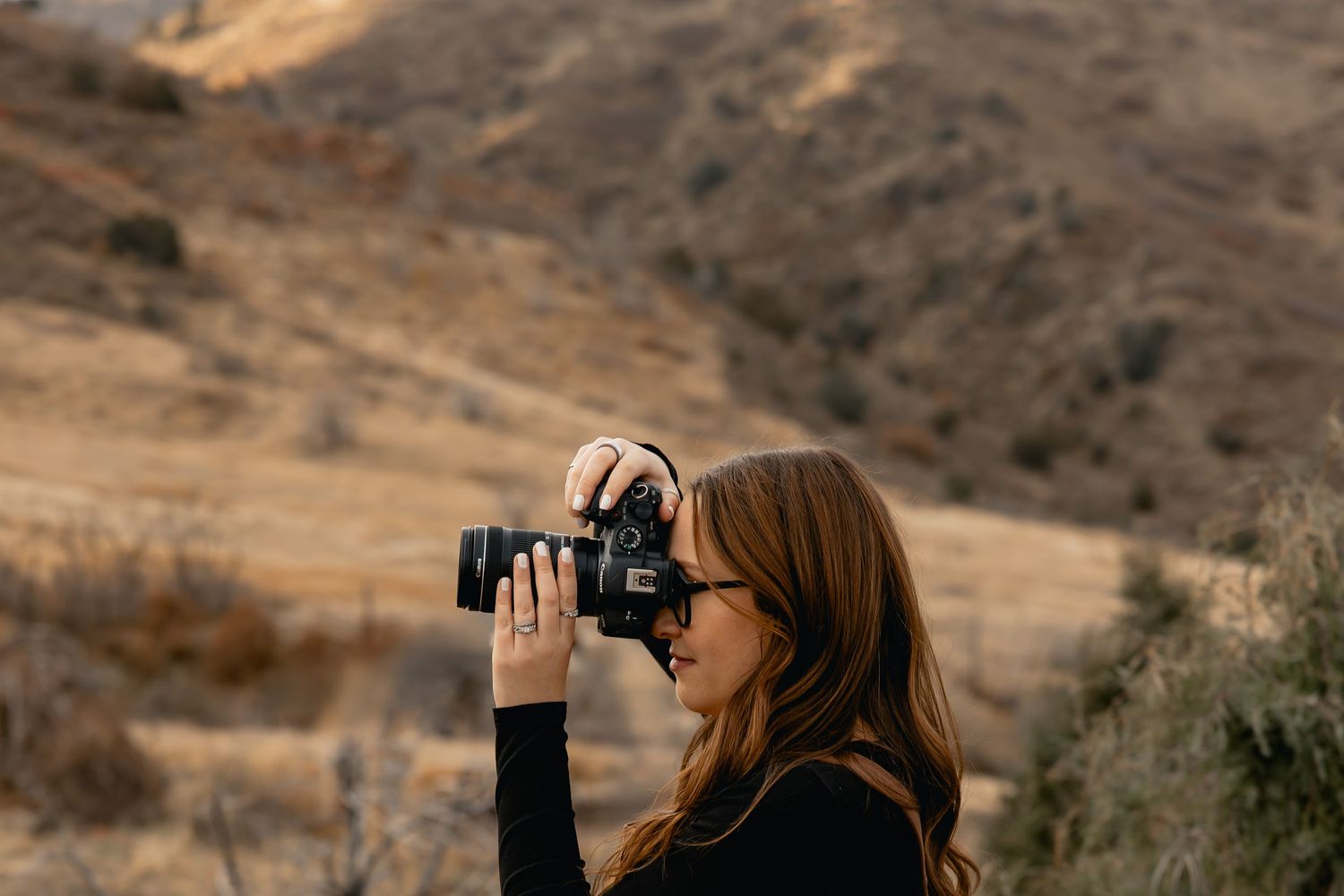 A person using binoculars to observe wildlife in a mountainous desert landscape during sunset.