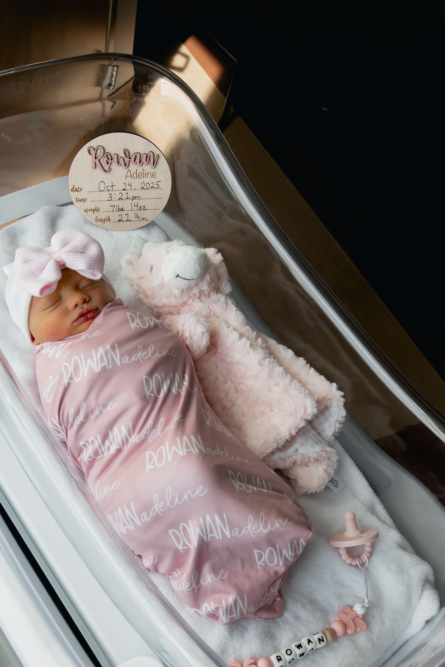 A newborn baby wearing a soft pink sleeper rests peacefully in a hospital bassinet.
