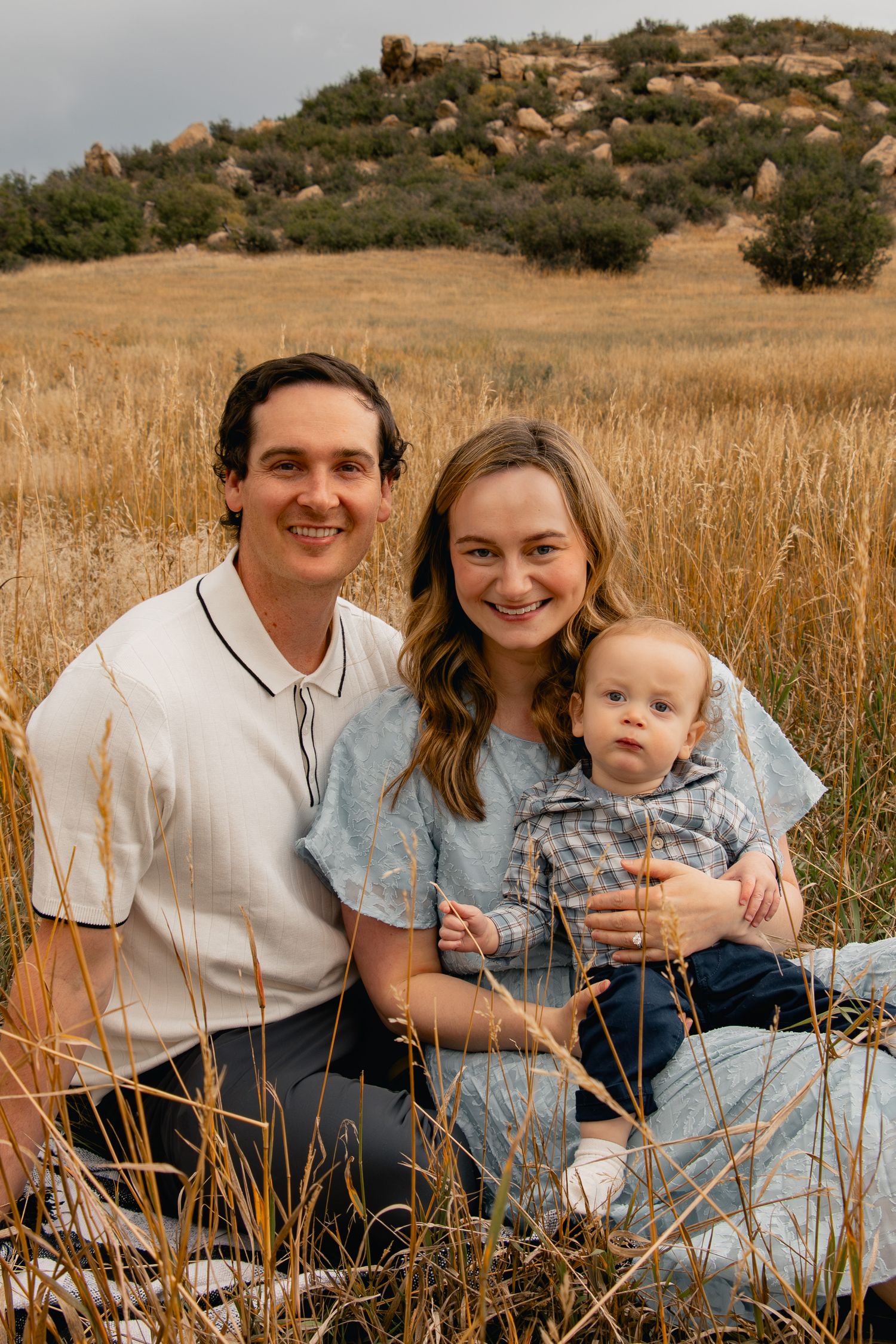 A small family sits together in a field of tall golden grass on a sunny afternoon.