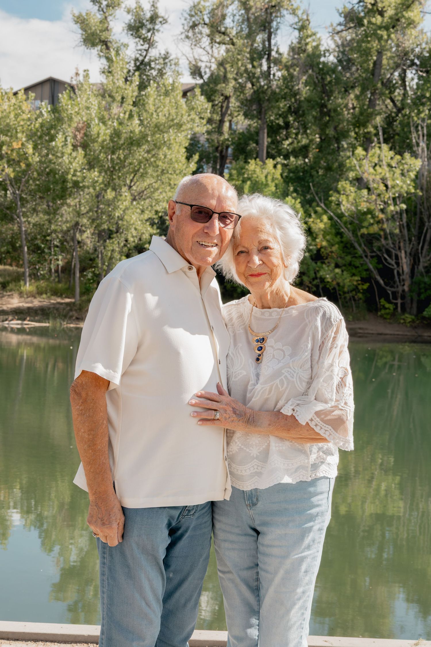 Two people sharing a joyful moment together by a tranquil lake surrounded by trees.