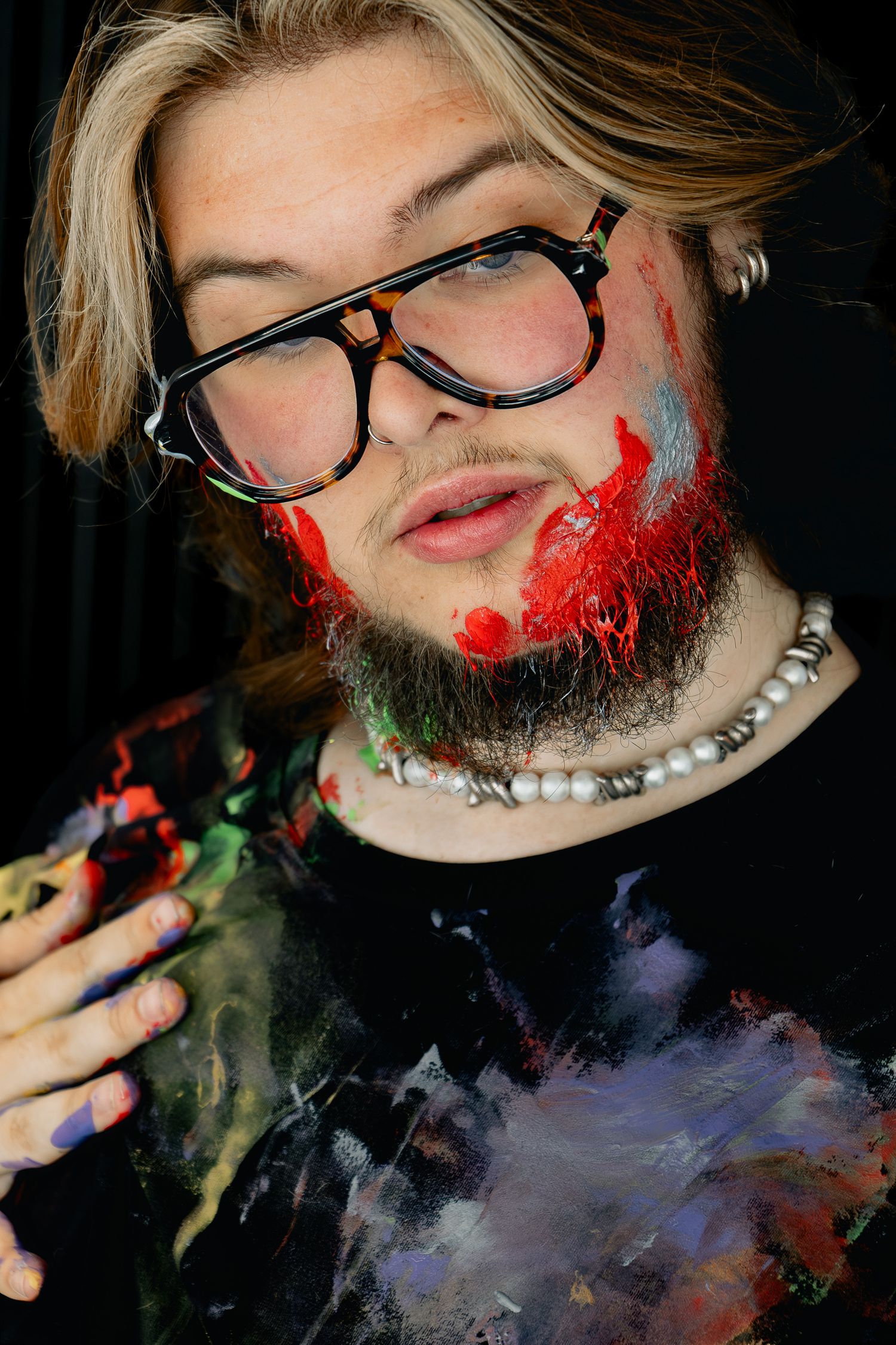 Artistic self-portrait sequence with red and green paint effects and glasses against black backdrop.
