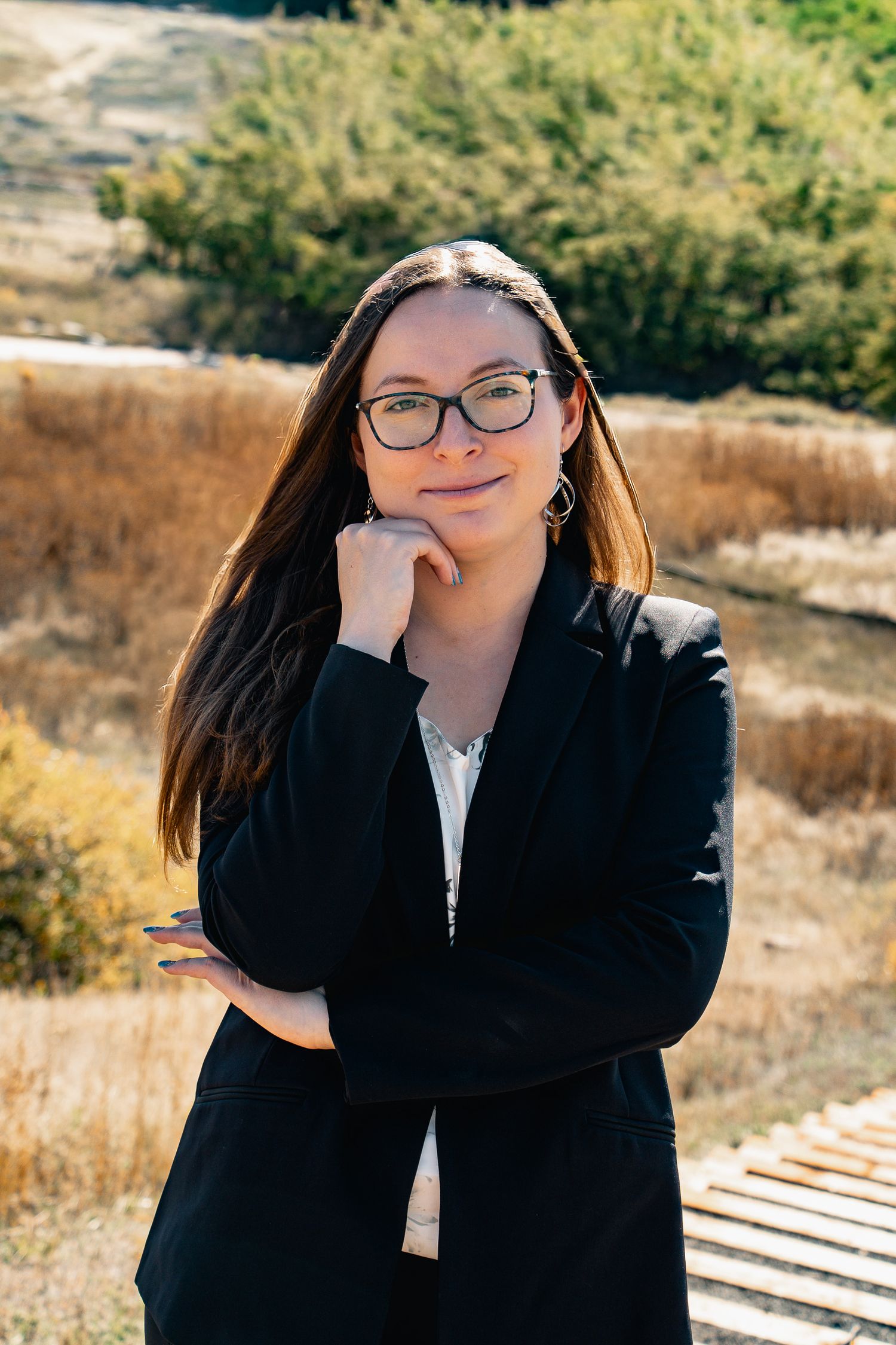 A series of outdoor portraits of a person in glasses and a black blazer posing against a natural backdrop.