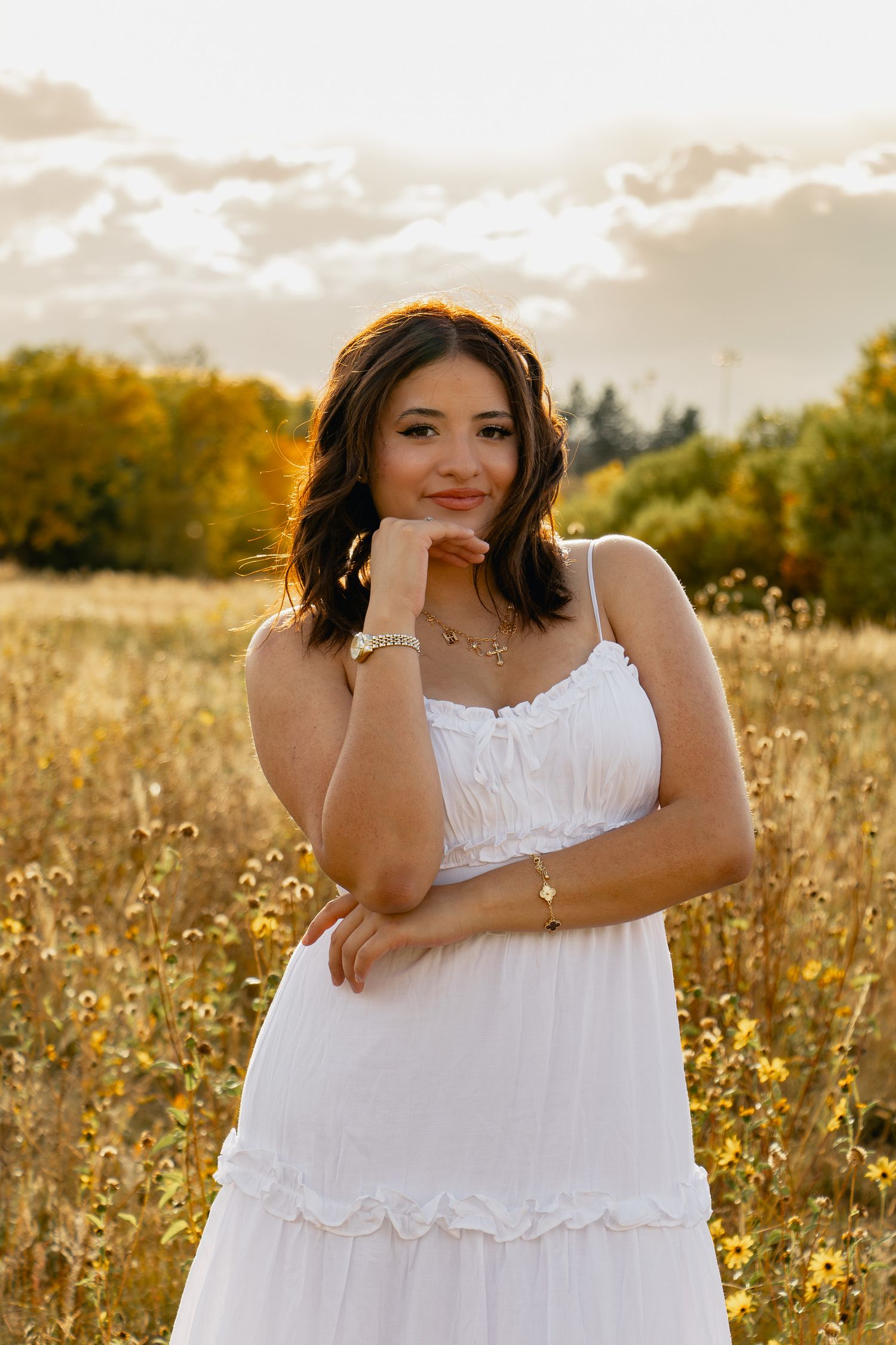 A woman in a white dress poses gracefully in a golden sunlit meadow during sunset.