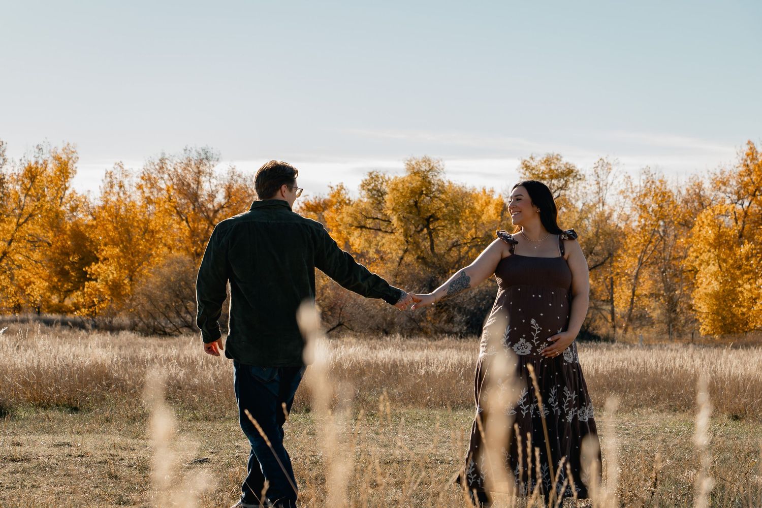 A couple walks hand in hand through a golden autumn field during sunset creating a romantic silhouette.
