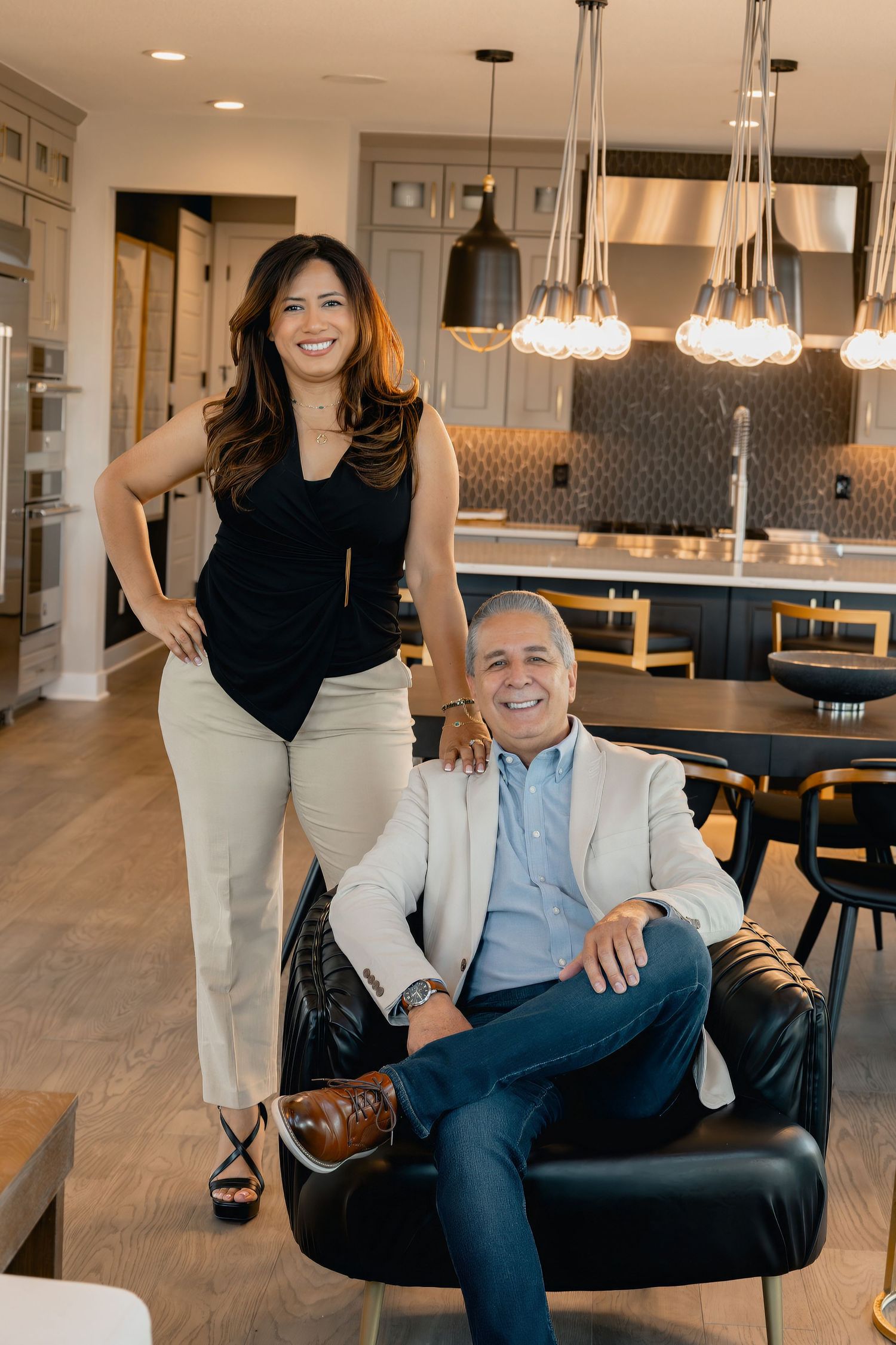 Two people smiling in a modern kitchen with pendant lighting and hardwood floors in a residential setting.
