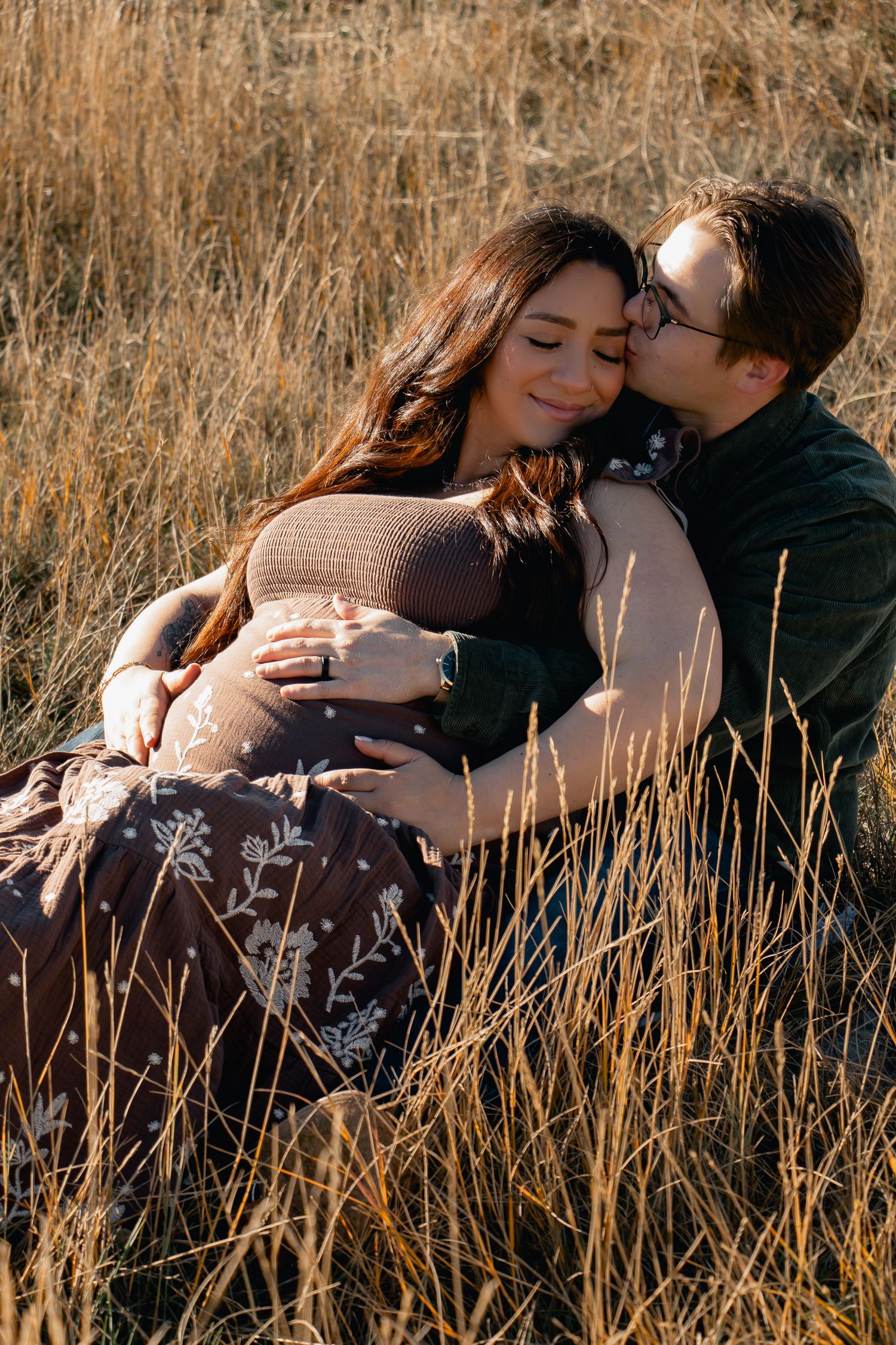 A romantic couple embraces in a golden field of tall grass during sunset.