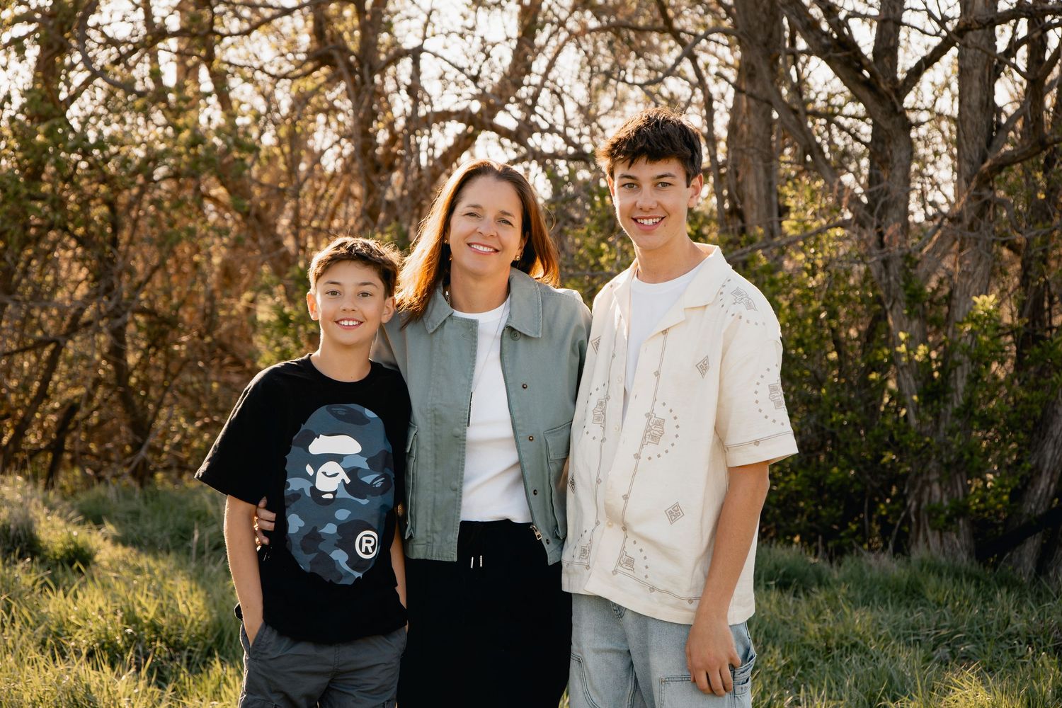 Three people pose together outdoors against a backdrop of autumn trees in warm natural lighting.