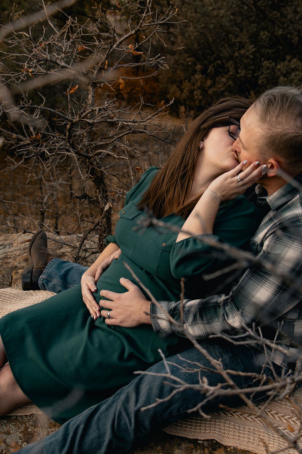 An intimate moment shared between two people lying on a textured blanket outdoors among autumn foliage.