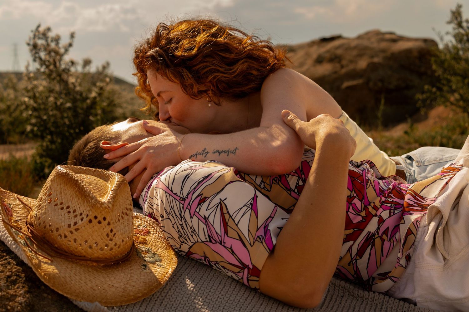 A couple relaxing outdoors on a blanket with golden light and rolling hills in the background.