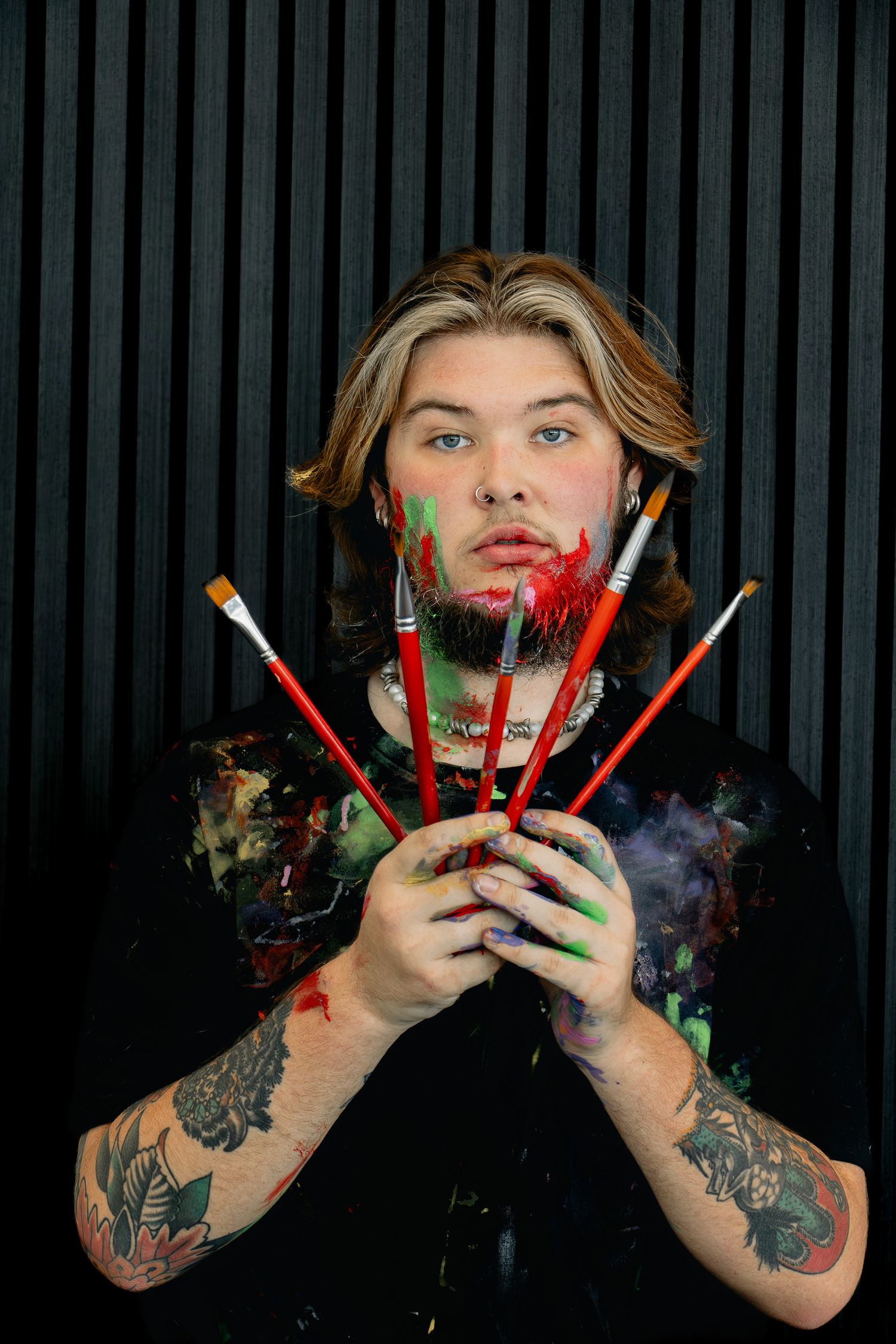 Creative portrait series showing hands holding colorful makeup brushes against dark background with smoke effects.