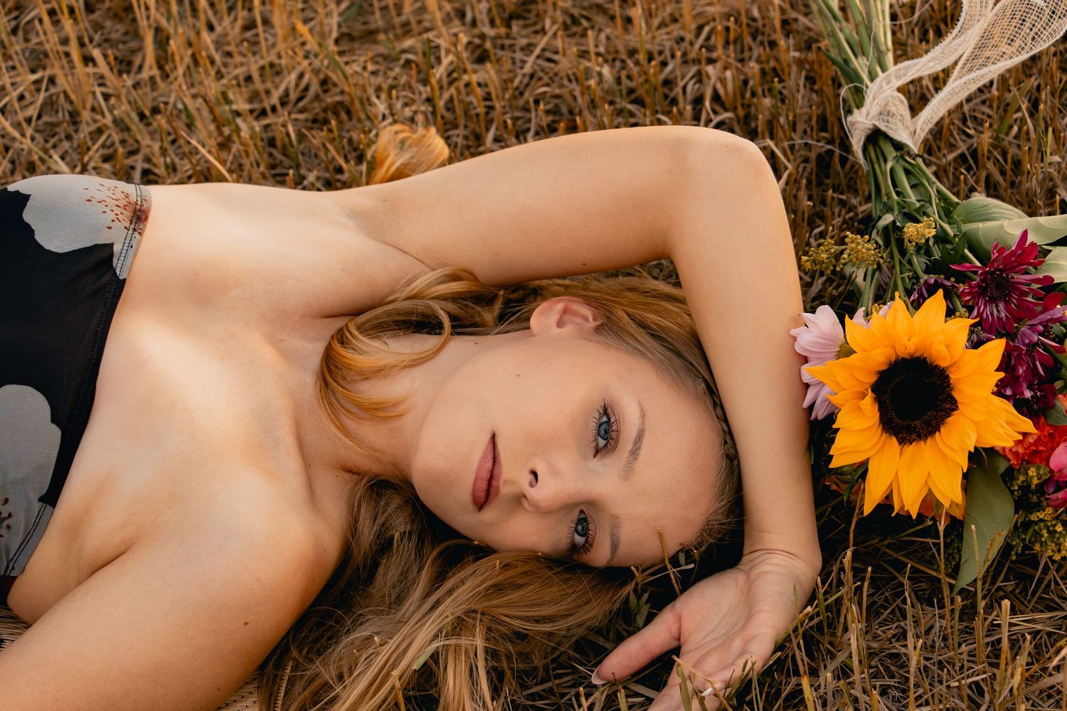 A lone sunflower sits beside someone lying in a golden grassy field during late summer.