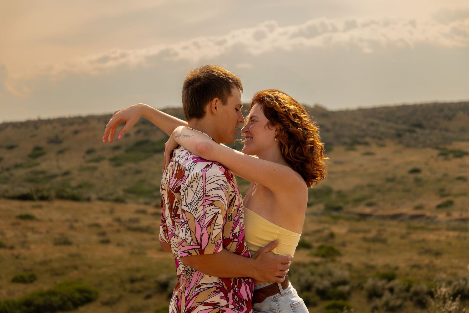 Romantic couple embraces during sunset in a desert landscape with warm golden light.