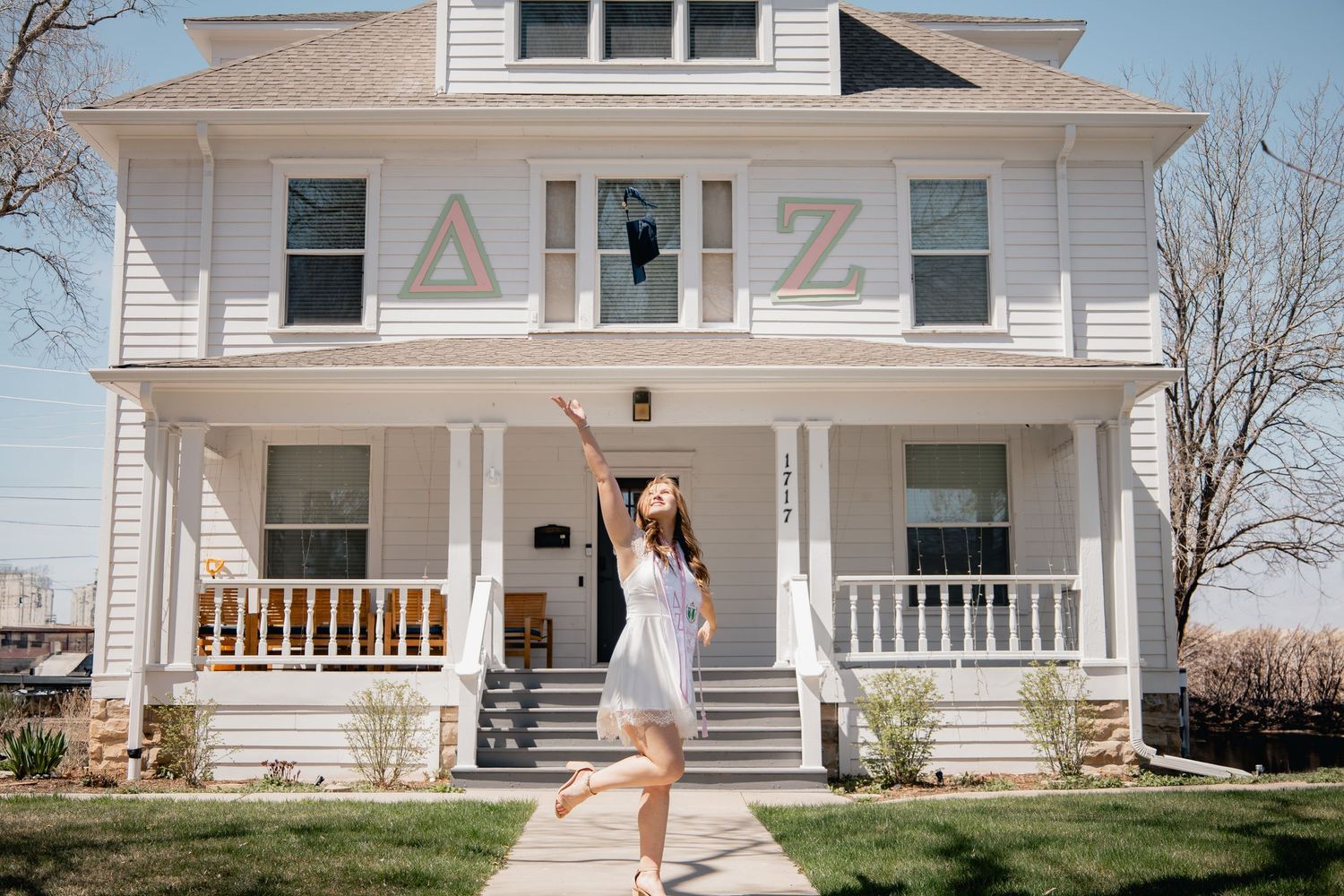 White sorority house with Greek letters Delta Zeta on the front porch as someone celebrates on the steps.