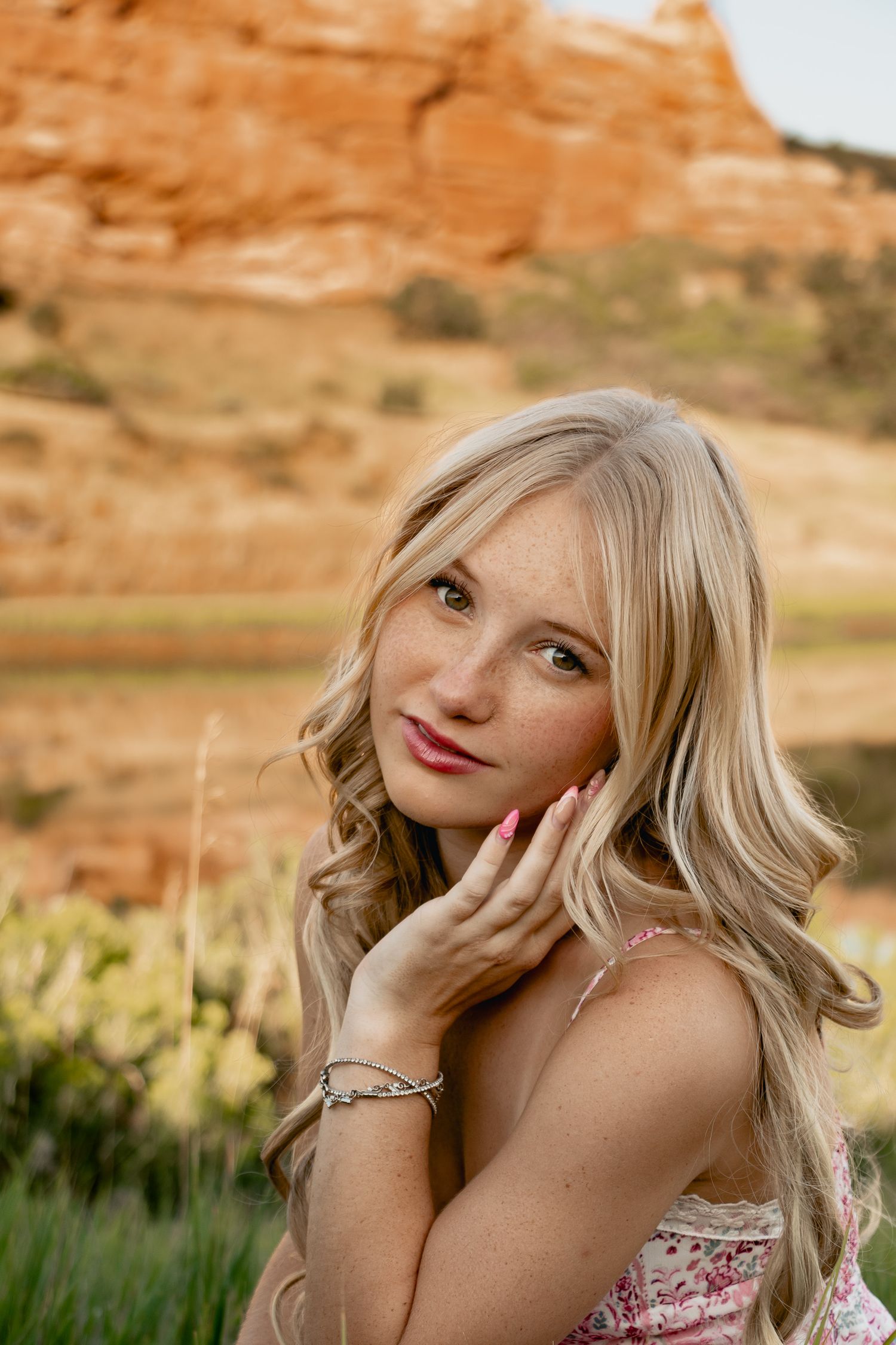 A person in a floral dress poses against red rock formations in warm sunlight while gazing upward dreamily.