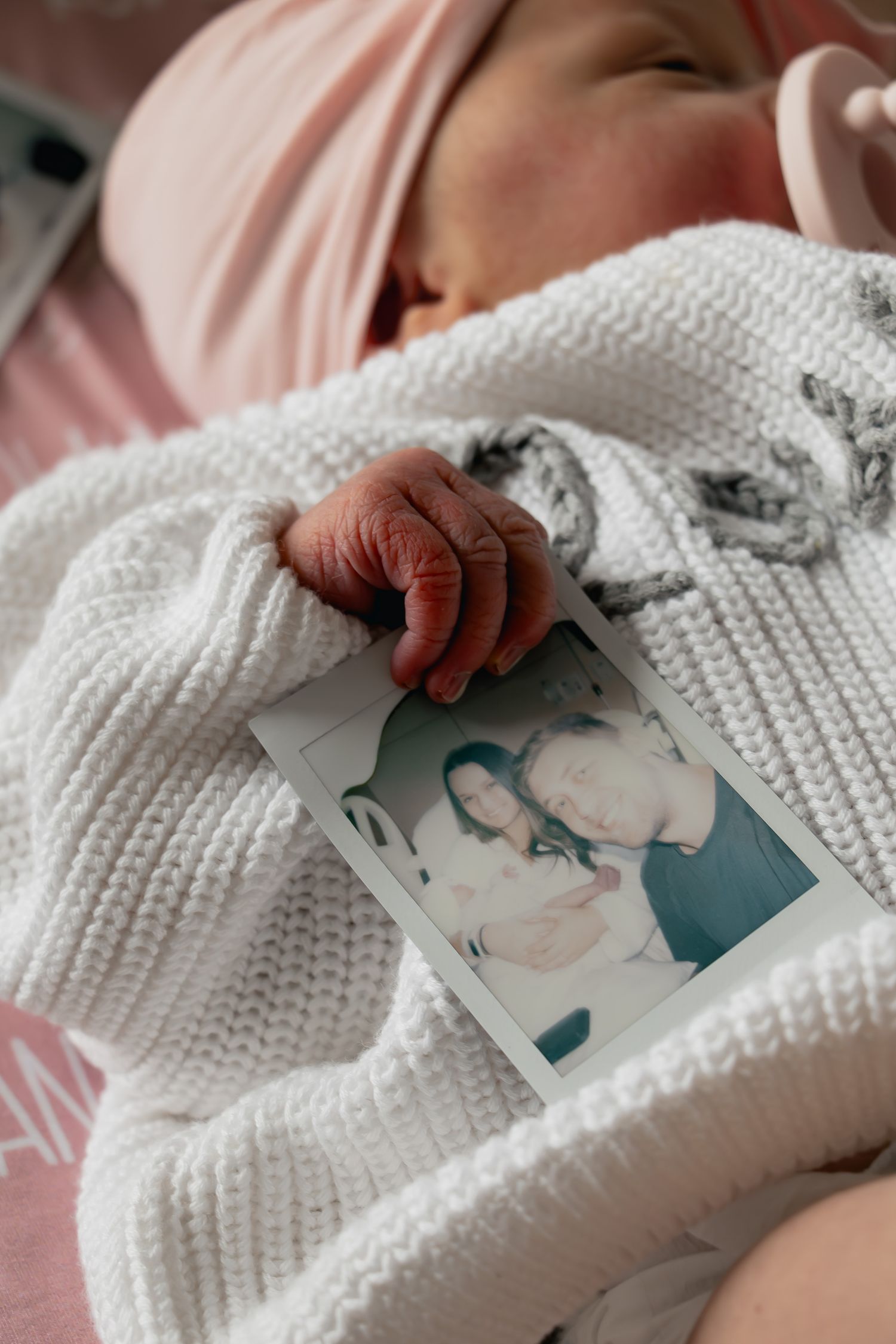 Hands holding a white knit blanket and looking at printed photographs in a cozy indoor setting.