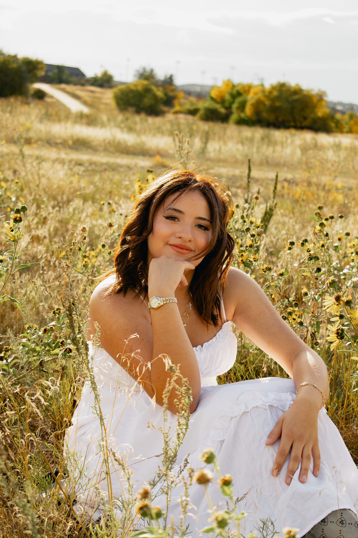 A person in a white dress poses in a golden field of wildflowers during sunset.